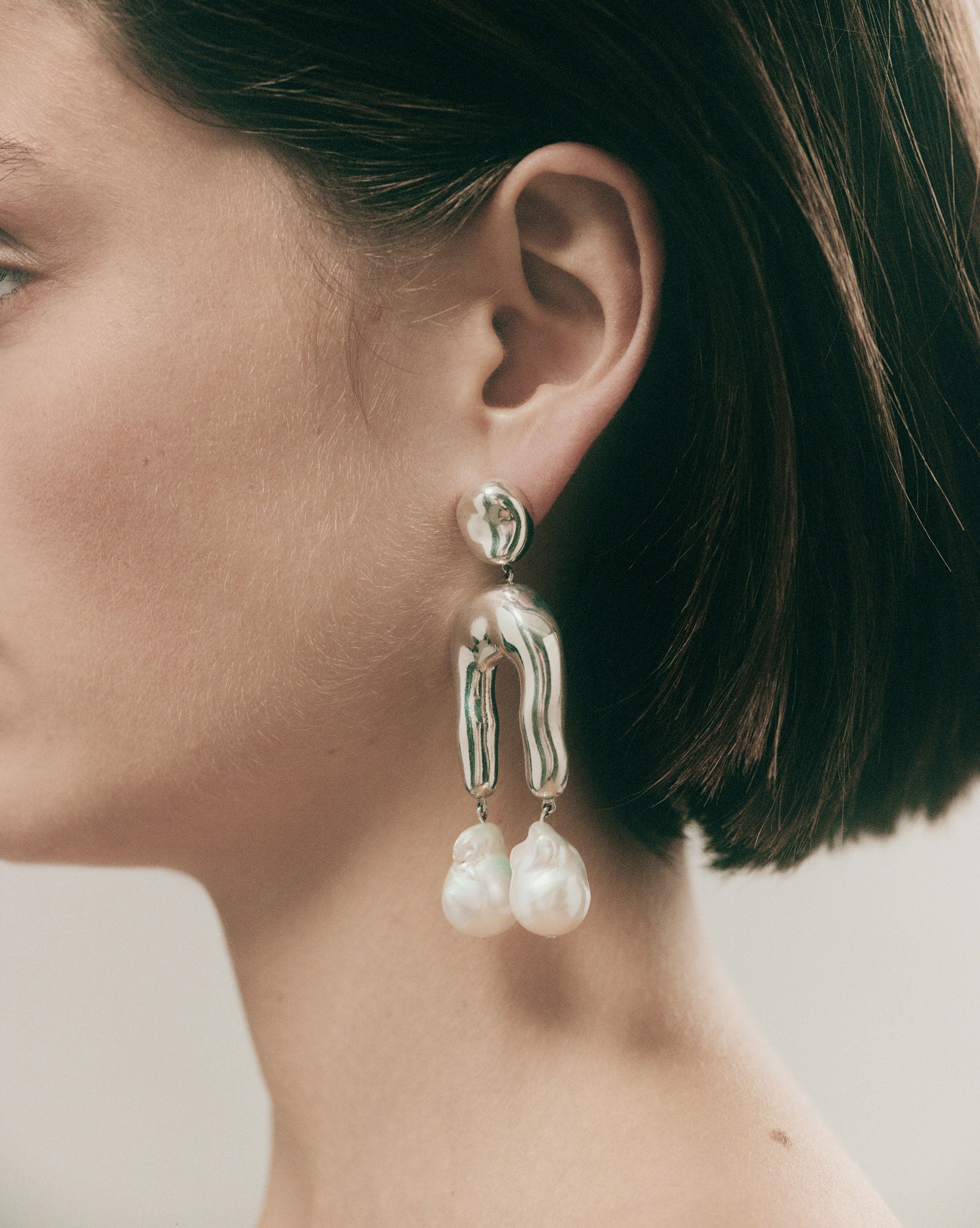 Woman wearing AGMES 0.925 sterling silver earrings with sculpted wishbone and freshwater pearl drop.