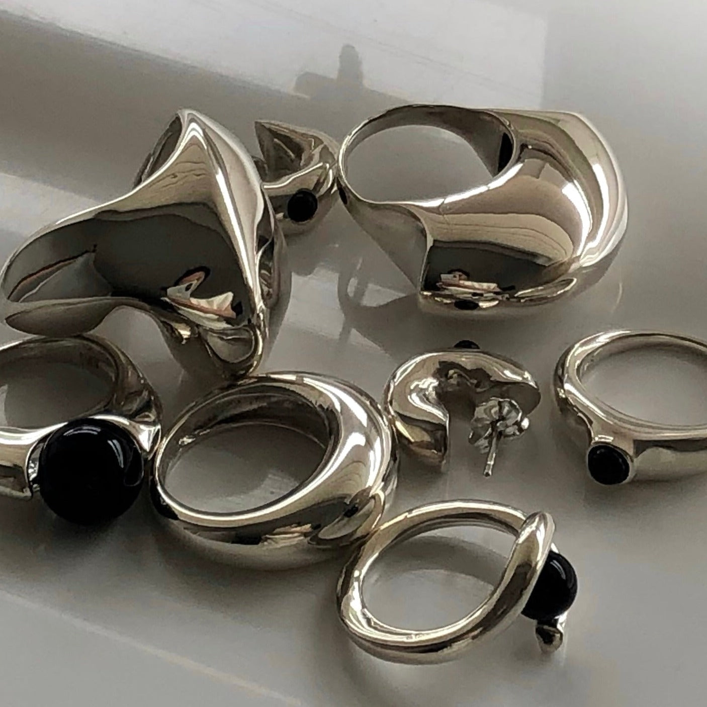 AGMES .925 Sterling Silver Jouve Ring, Turner Ring, Domed Ring, Claire Ring, Cara Ring, Chloe Ring, and Logan Hoops pictured on white reflective surface.