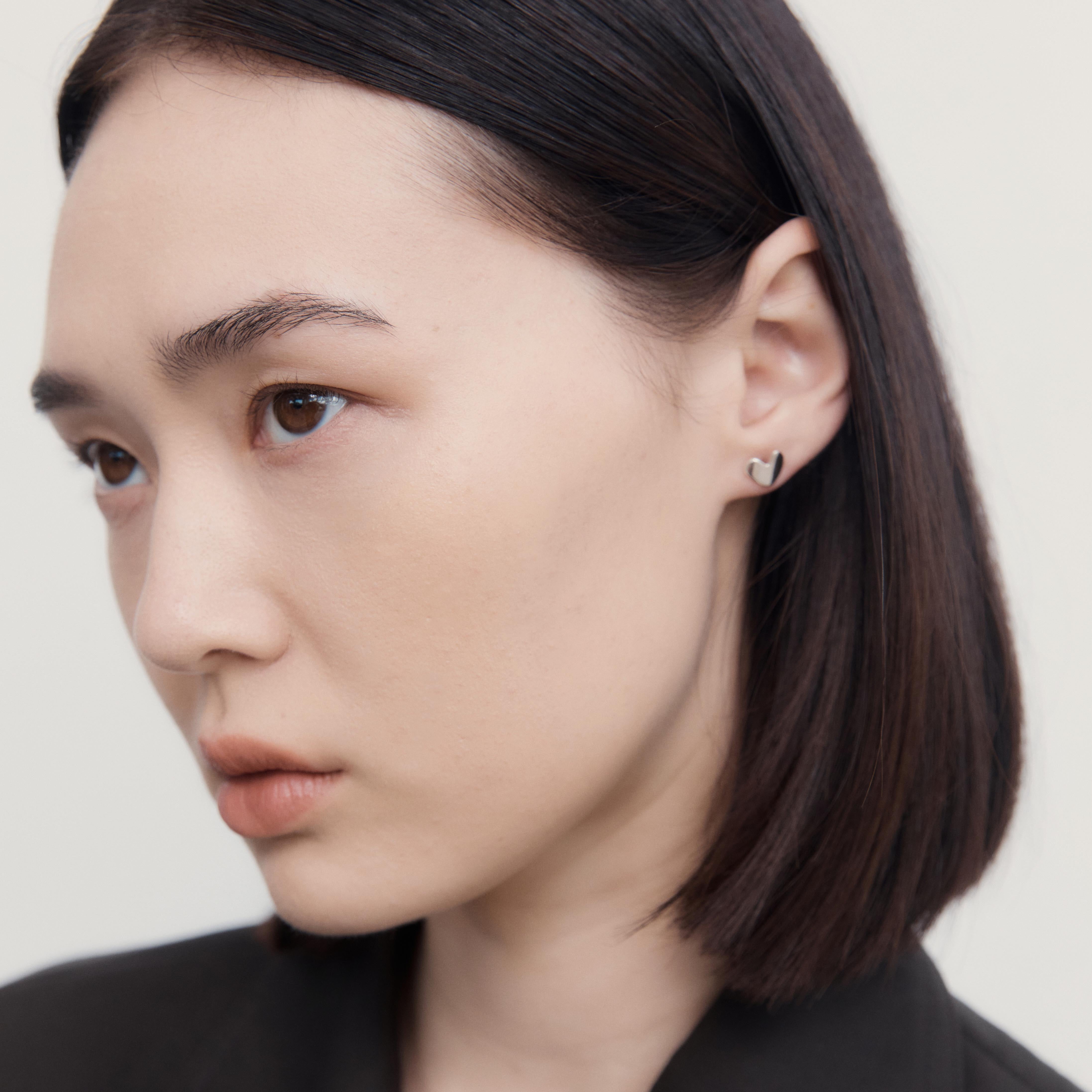 Woman wearing AGMES 0.925 sterling silver sculpted heart stud earrings.