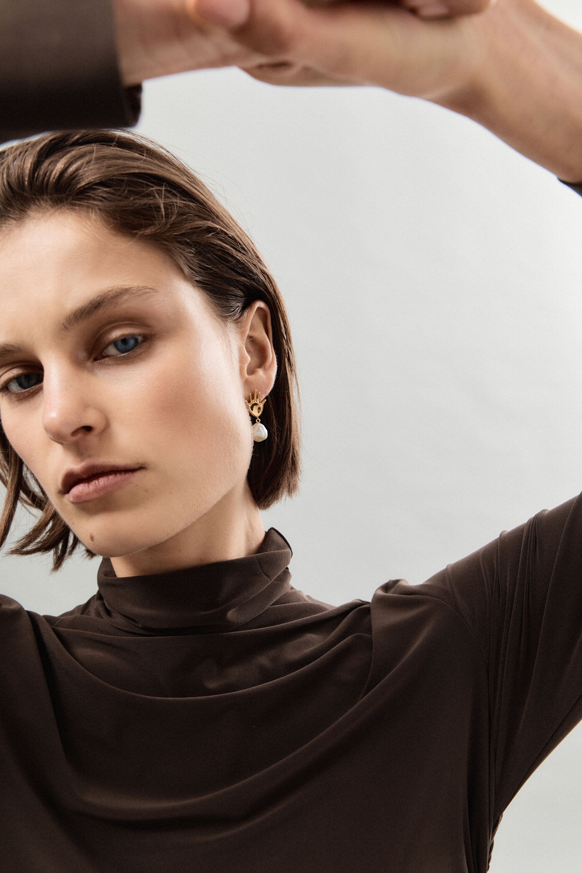 Woman wearing AGMES 18k gold vermeil abstract hand earrings with baroque freshwater pearl drop.