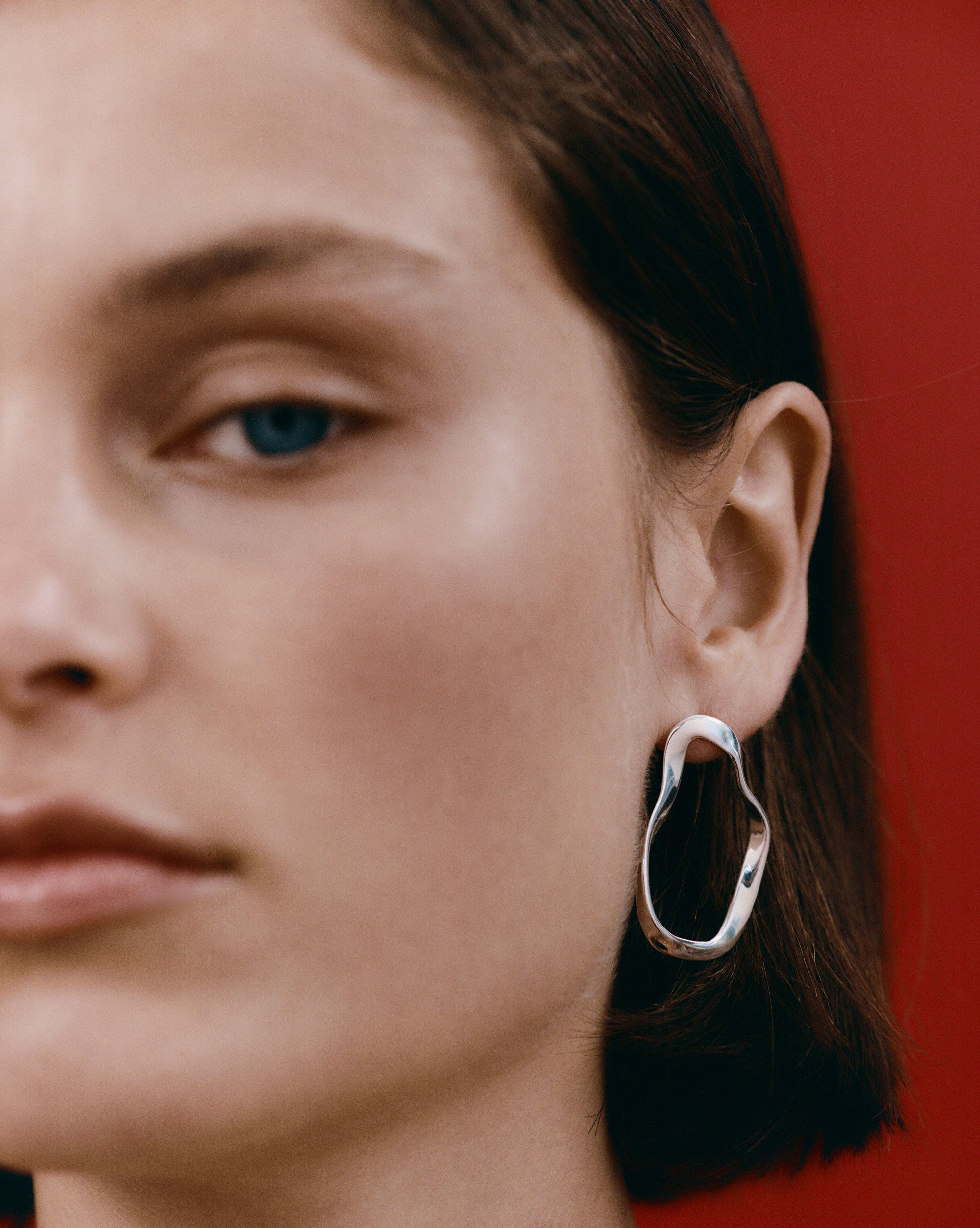 Woman wearing AGMES 0.925 sterling silver sculptural wavy small round hoop earrings.