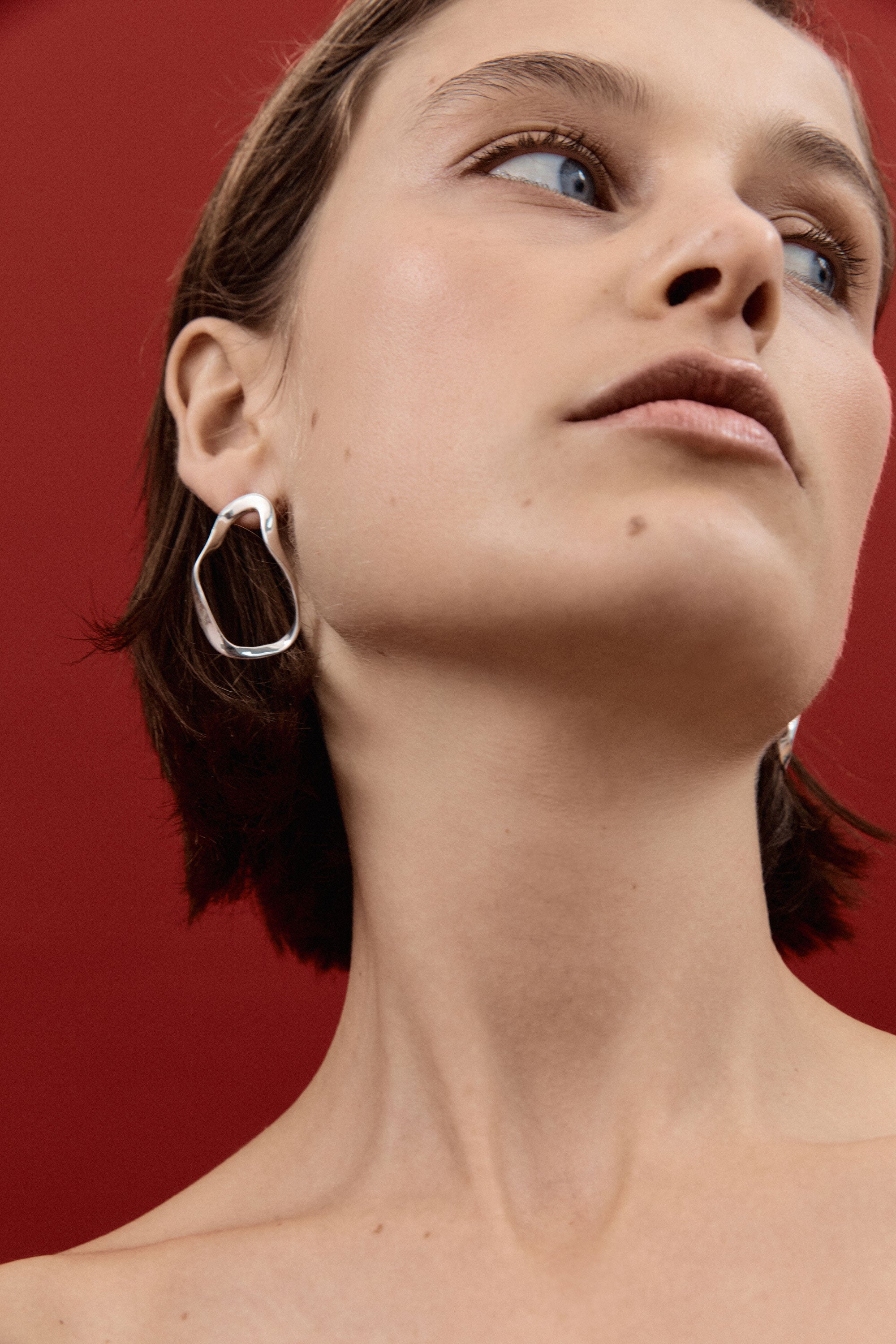 Woman wearing AGMES 0.925 sterling silver sculptural wavy small round hoop earrings.