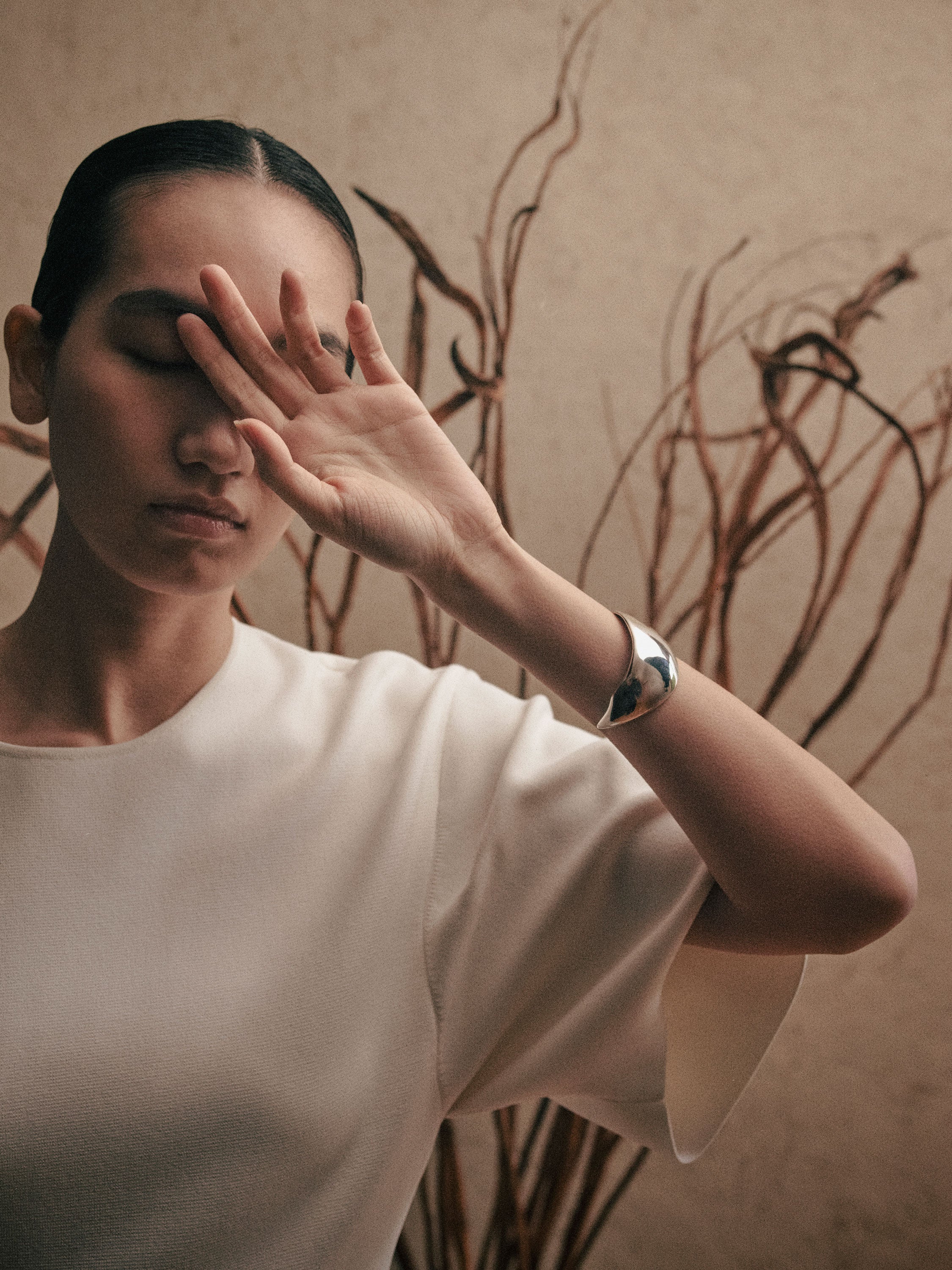 Woman wearing white blouse and AGMES 0.925 sterling silver sculpted Cecil cuff bracelet with natural background.