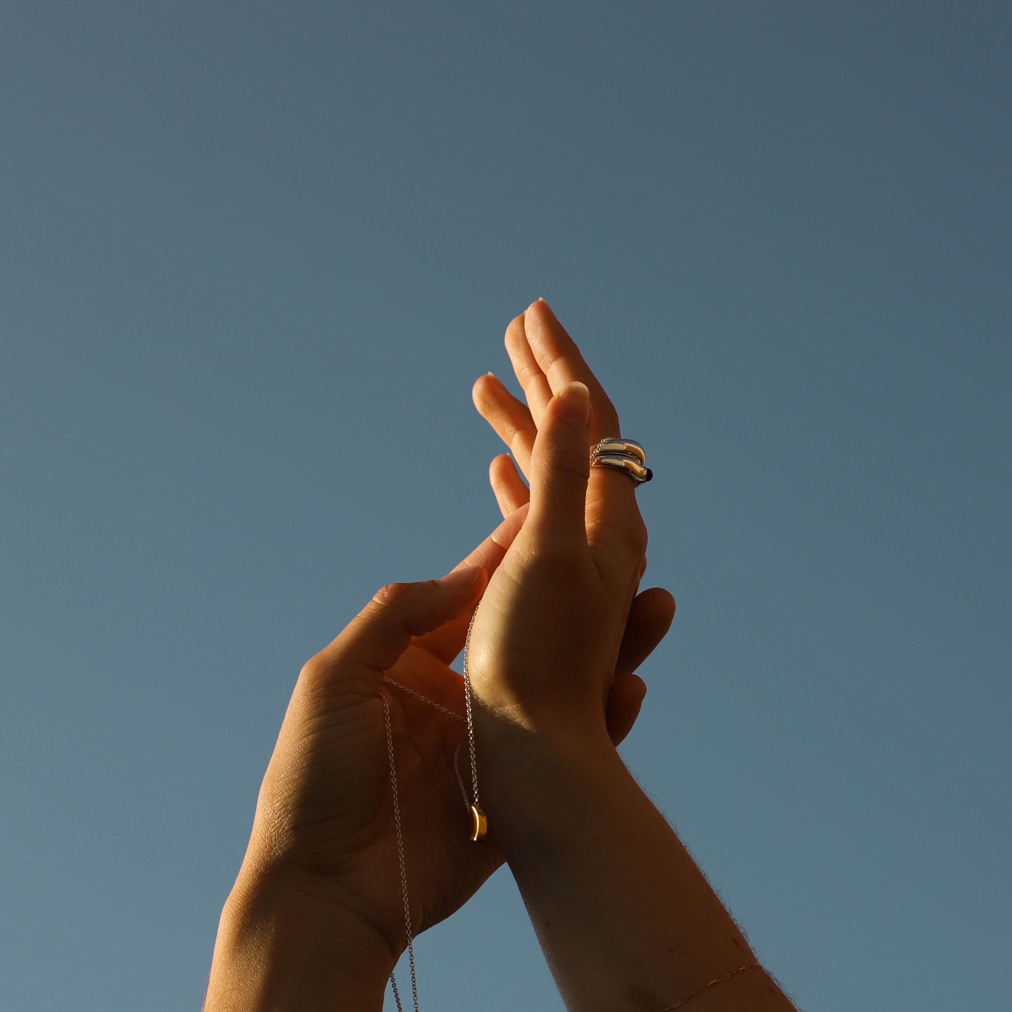 AGMES 18K Gold Vermeil Pendant. Modern connecting heart necklace. Displayed on hand facing the sky.