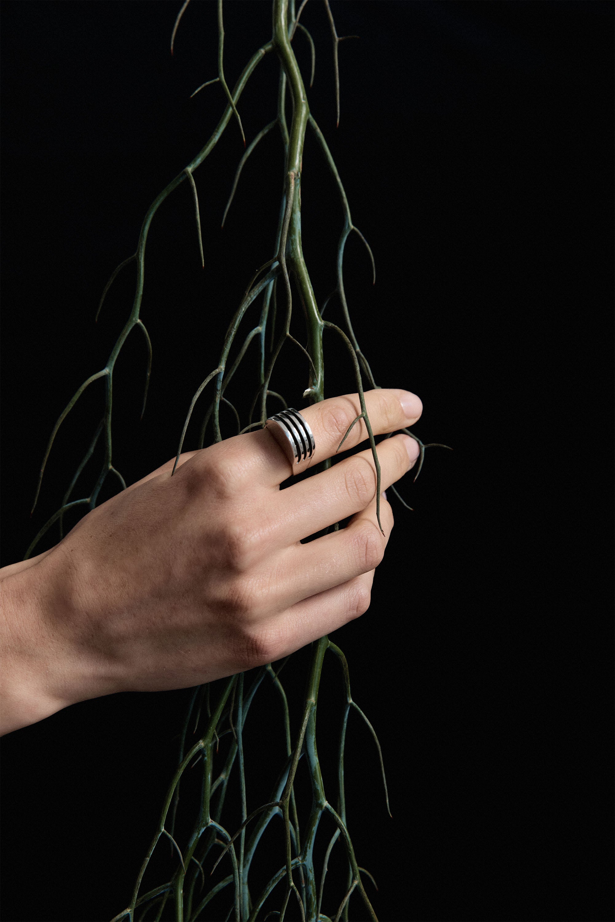 Hand wearing AGMES .925 Sterling Silver Boeri Ring and holding branch on black background.