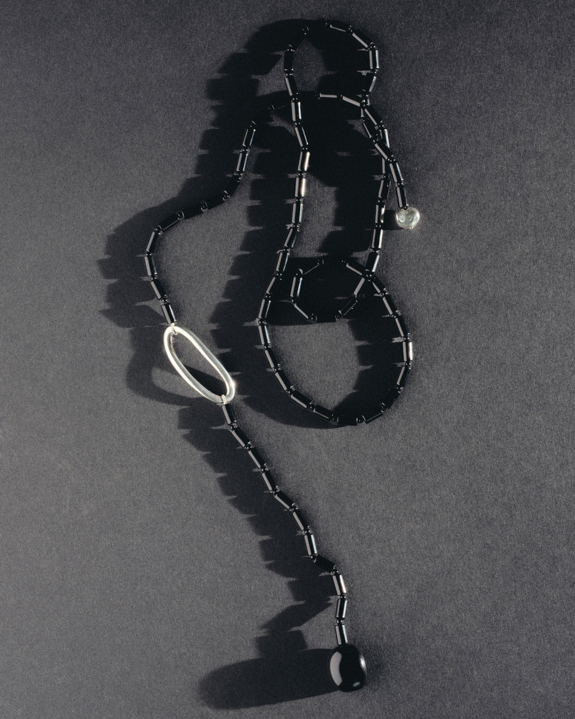 Black Onyx beaded lasso lariat style necklace with sterling silver accents laying on grey surface