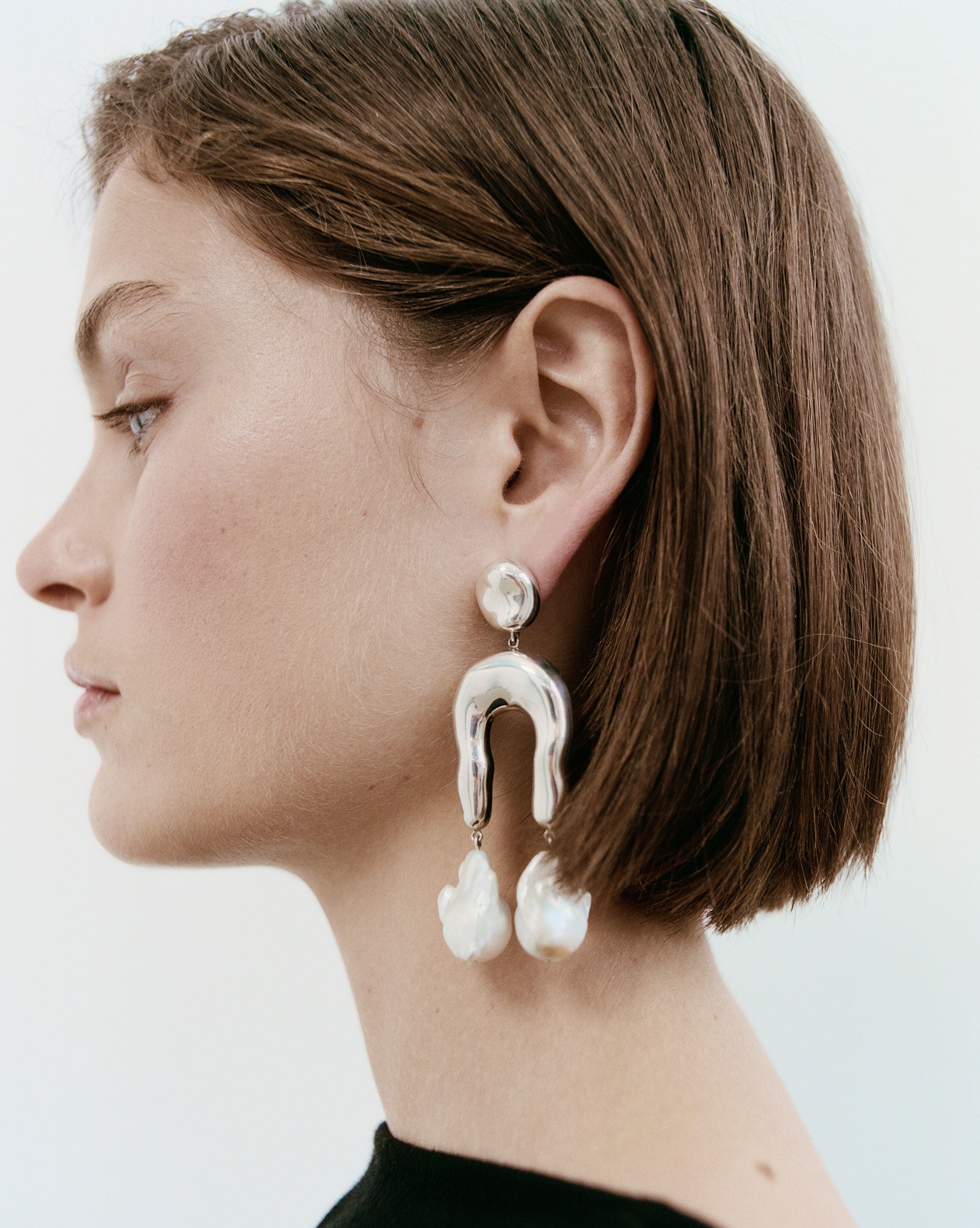 Woman wearing AGMES 0.925 sterling silver earrings with sculpted wishbone and freshwater pearl drop.