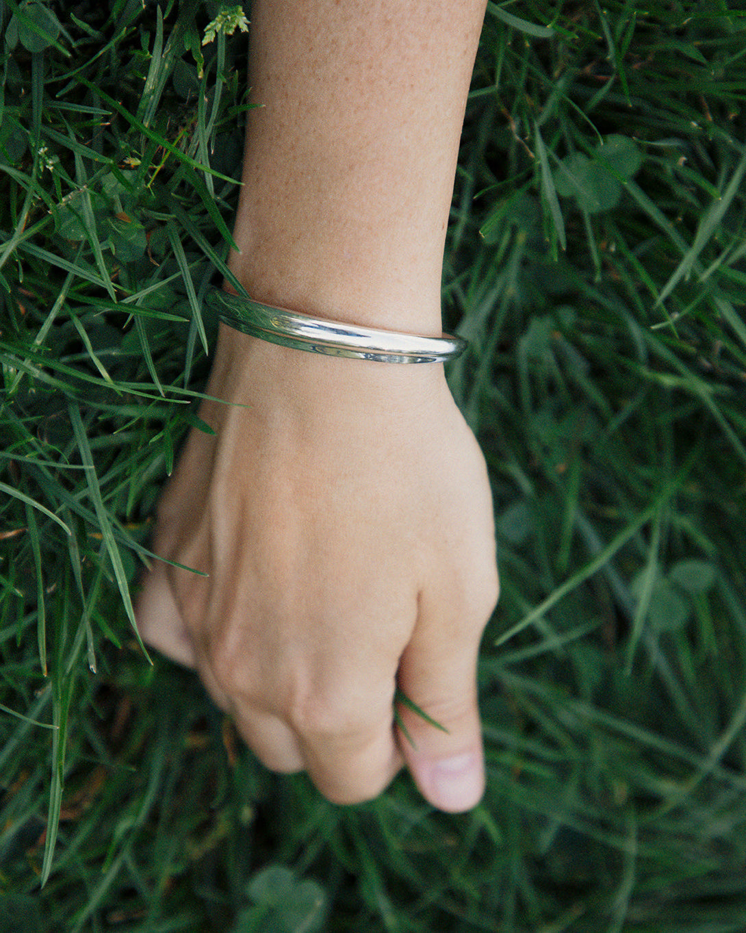 Model wearing AGMES .925 sterling silver thin, ridged, sculptural Cyril Cuff bracelet in grass.