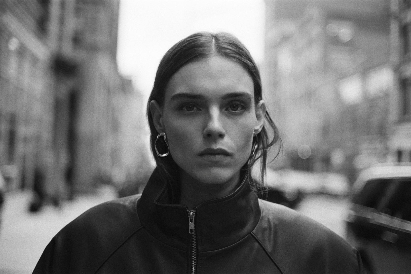 Model wearing AGMES .925 sterling silver sculptural round Small Vera Earrings with black leather jacket. Black and white image.