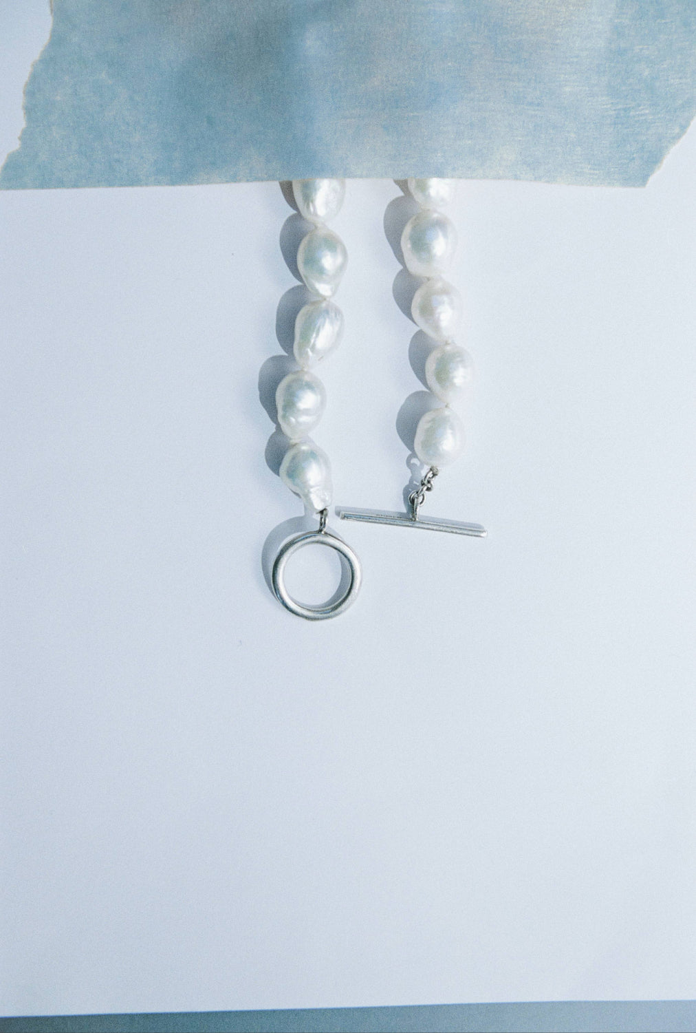 AGMES .925 sterling silver and baroque freshwater pearl necklace on light blue backgorund.