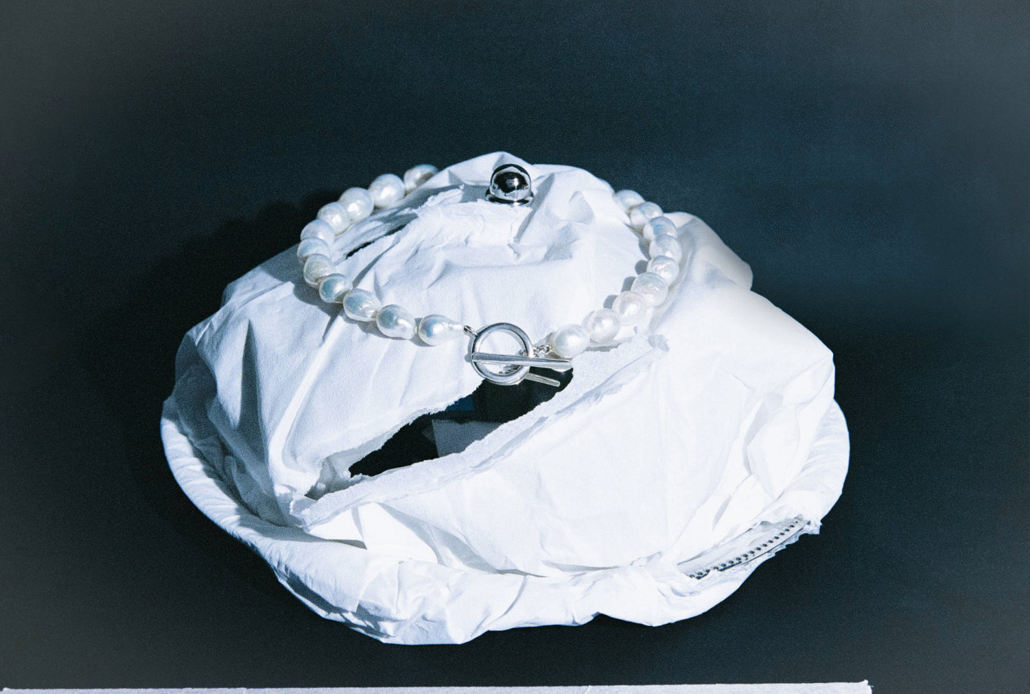 AGMES .925 sterling silver and baroque freshwater pearl necklace. Dark blue background and white fabric structure.