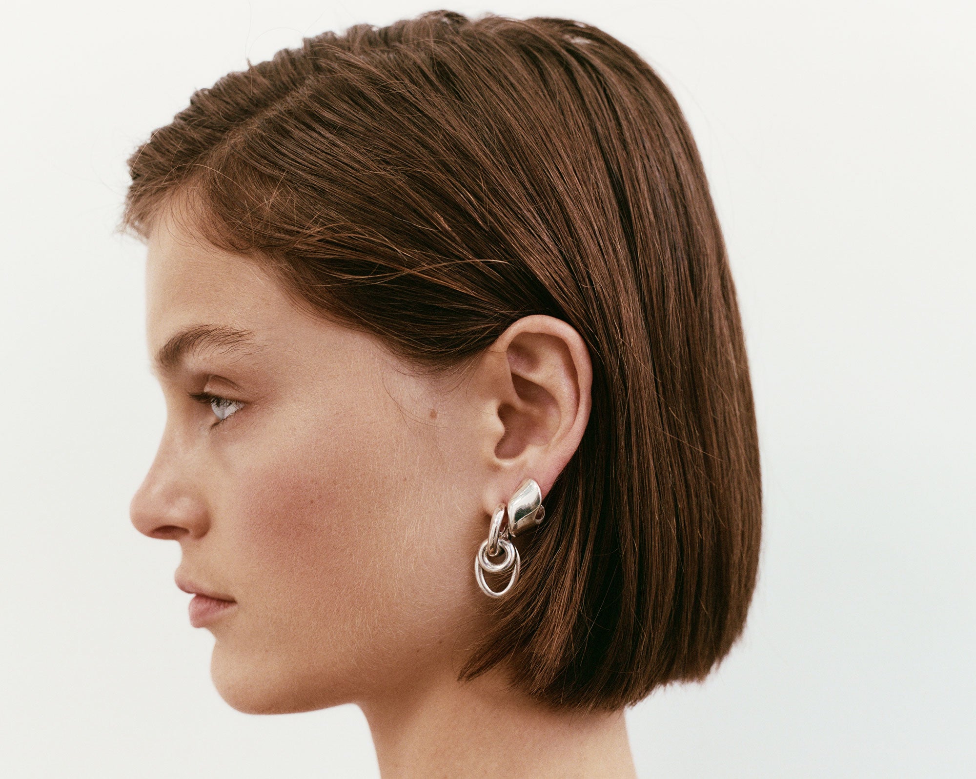 Woman wearing the AGMES .925 Sterling Silver Nelle Hoop Earrings. Asymmetrical mirrored hoops.