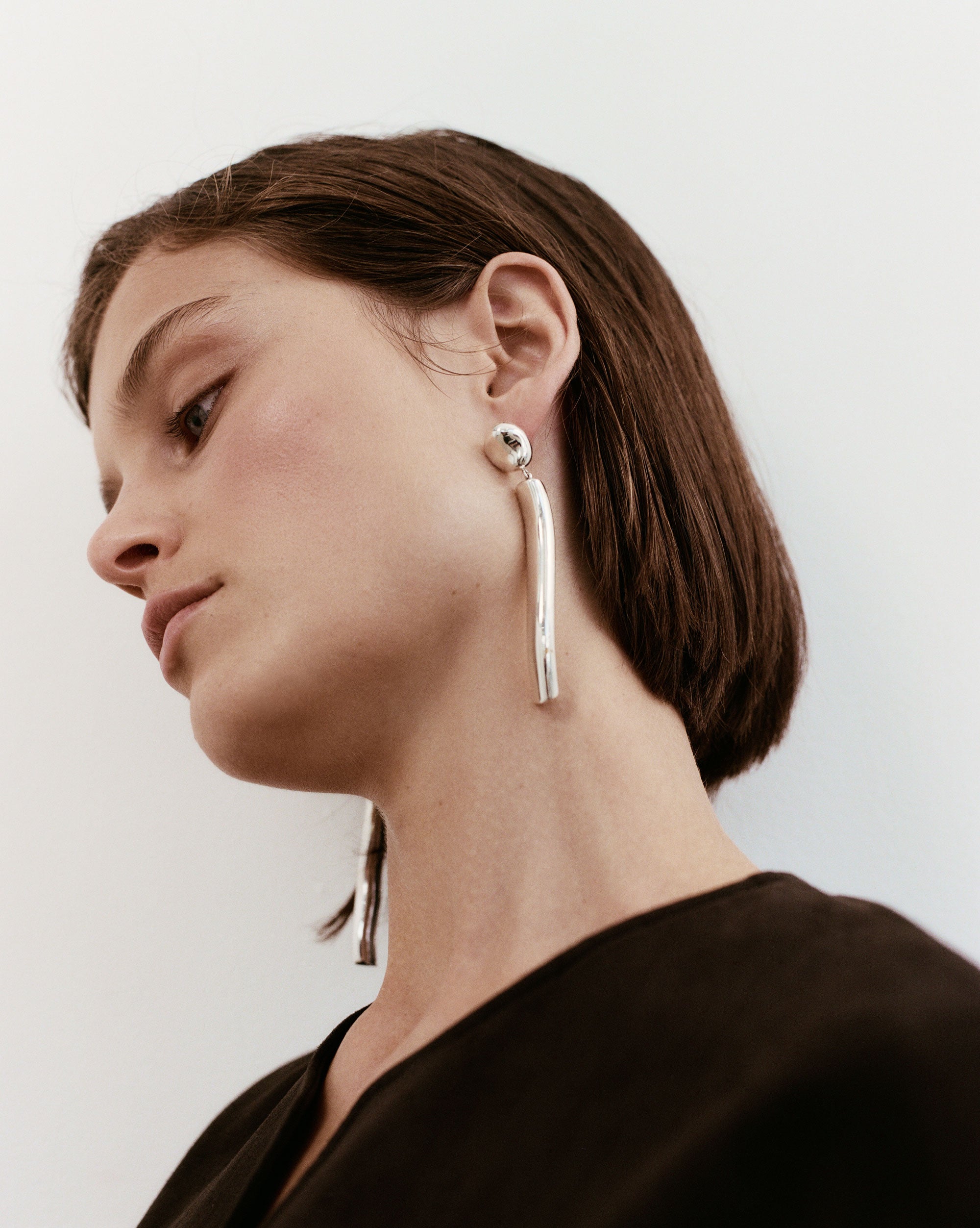 Woman wearing AGMES 0.925 sterling silver long sculptural drop earrings with silver top.