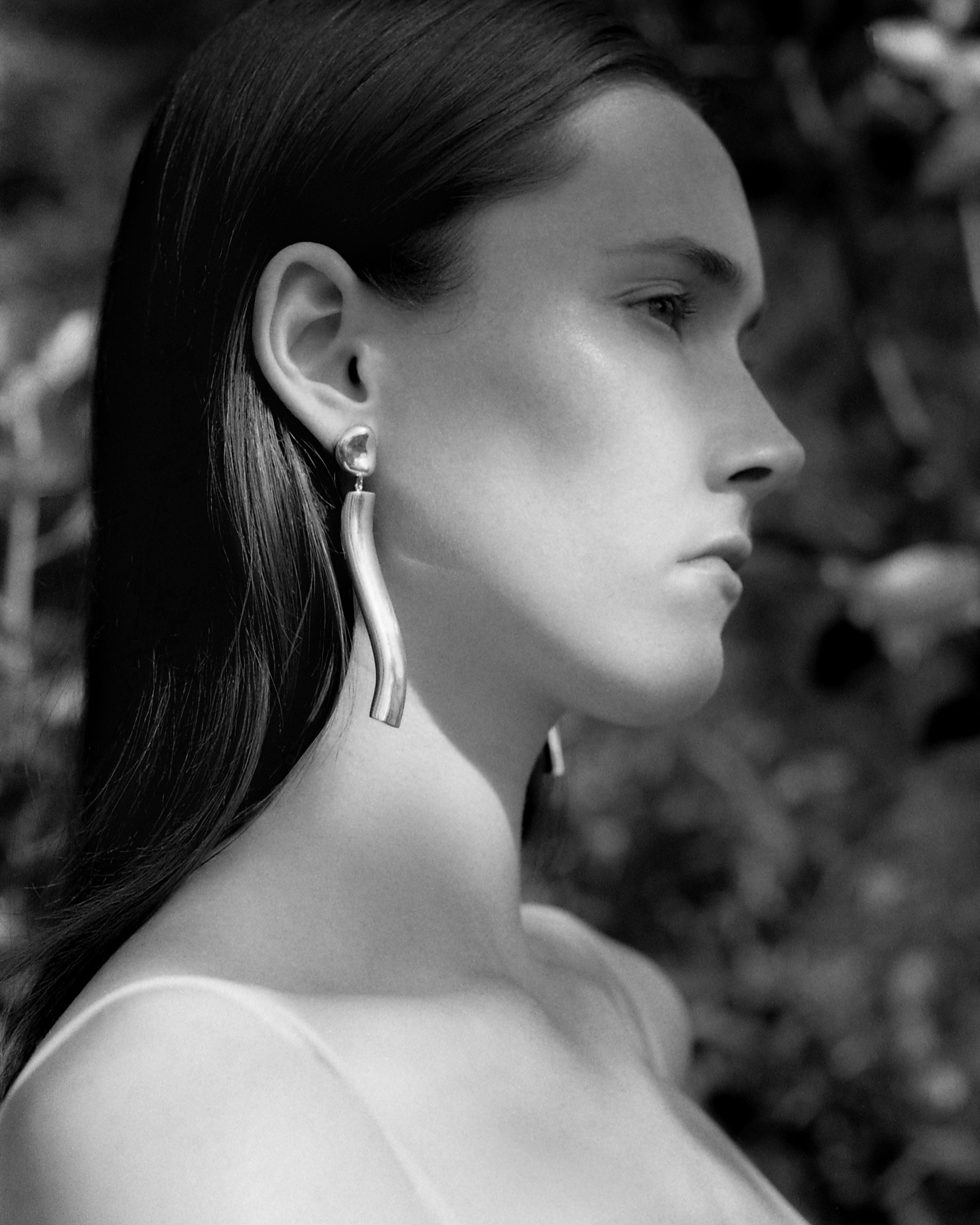 Woman wearing AGMES 0.925 sterling silver long sculptural drop earrings with silver top.