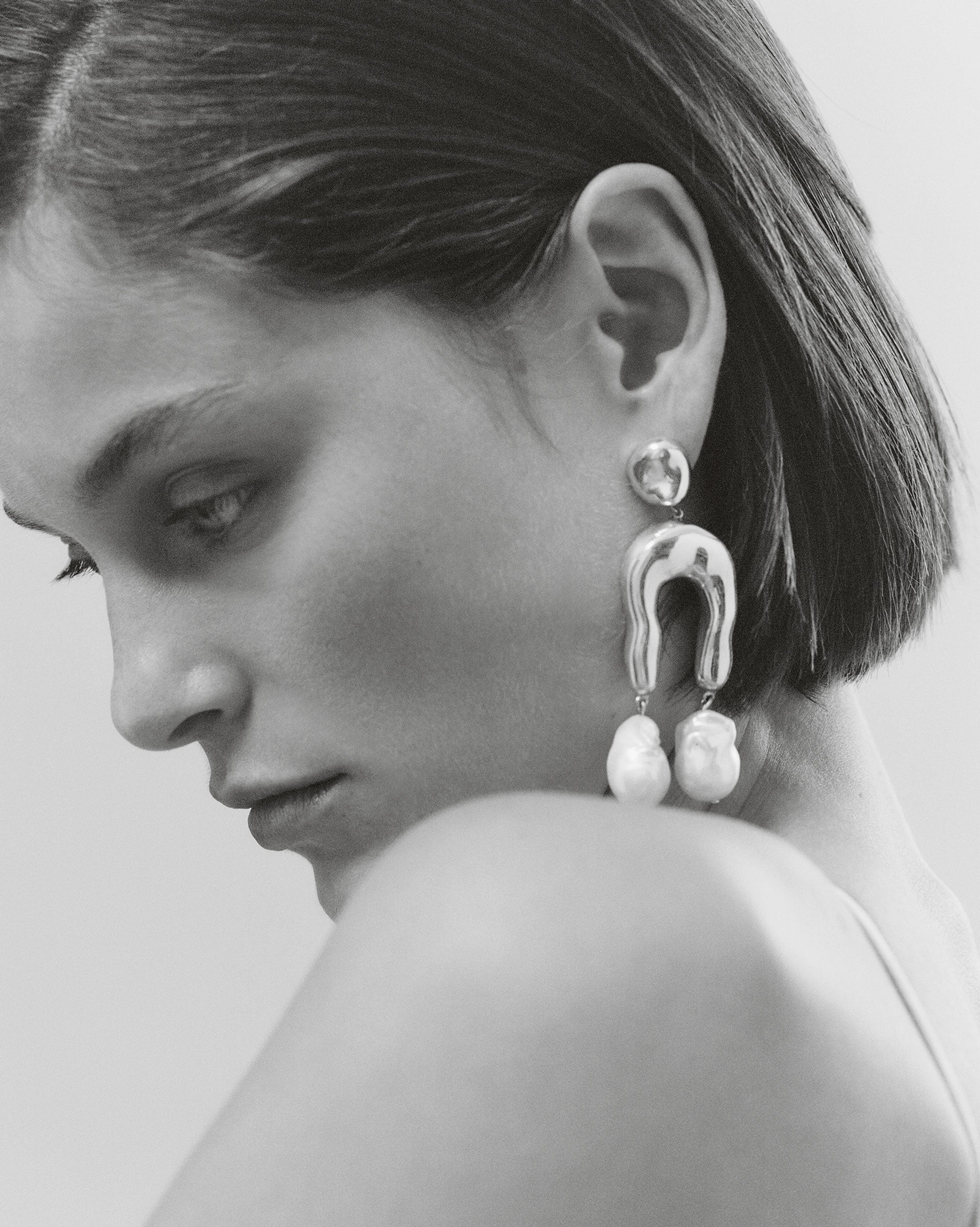 Woman wearing AGMES 0.925 sterling silver earrings with sculpted wishbone and freshwater pearl drop.