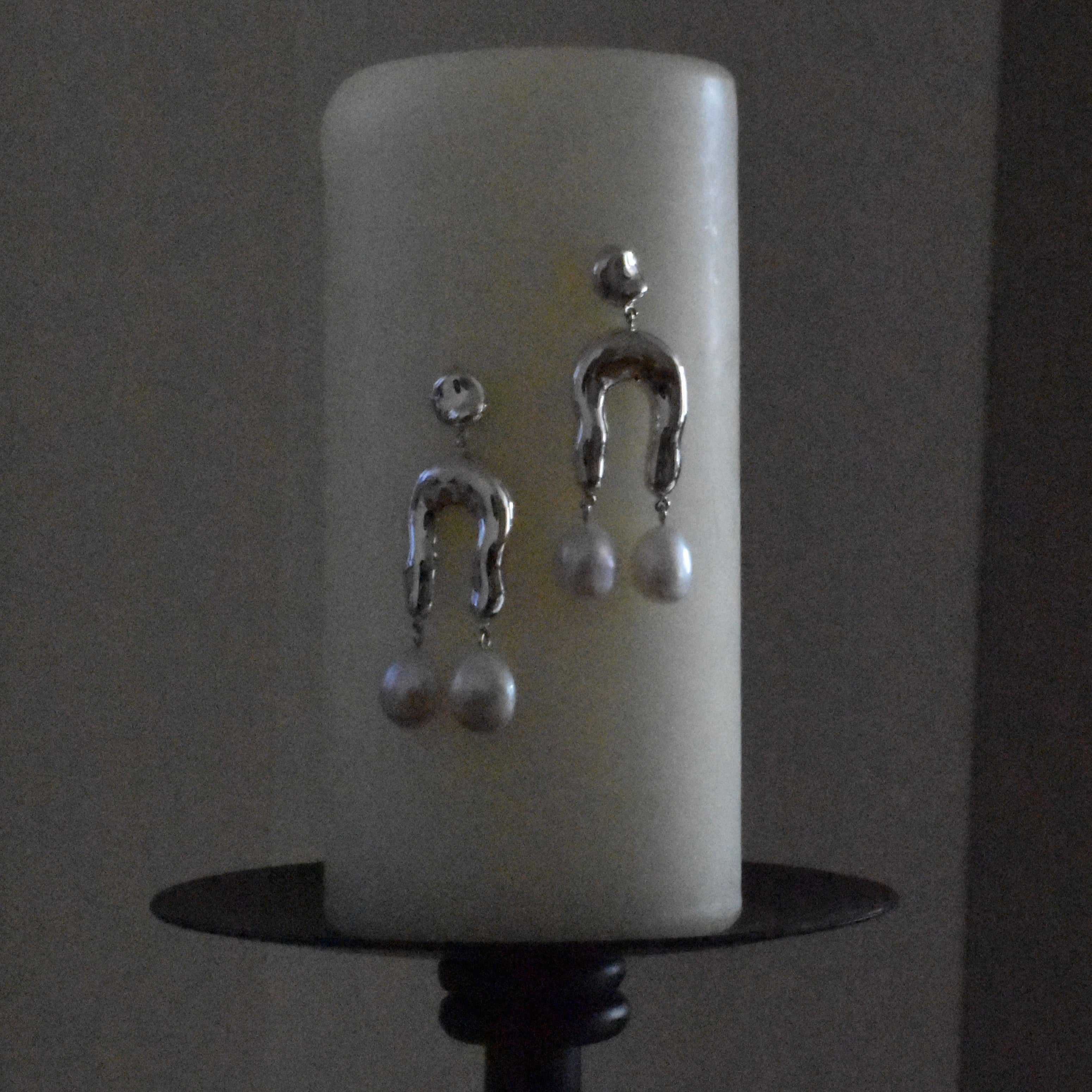 AGMES 0.925 sterling silver earrings with sculpted wishbone and freshwater pearl drop. Hanging in front of pillar candle.