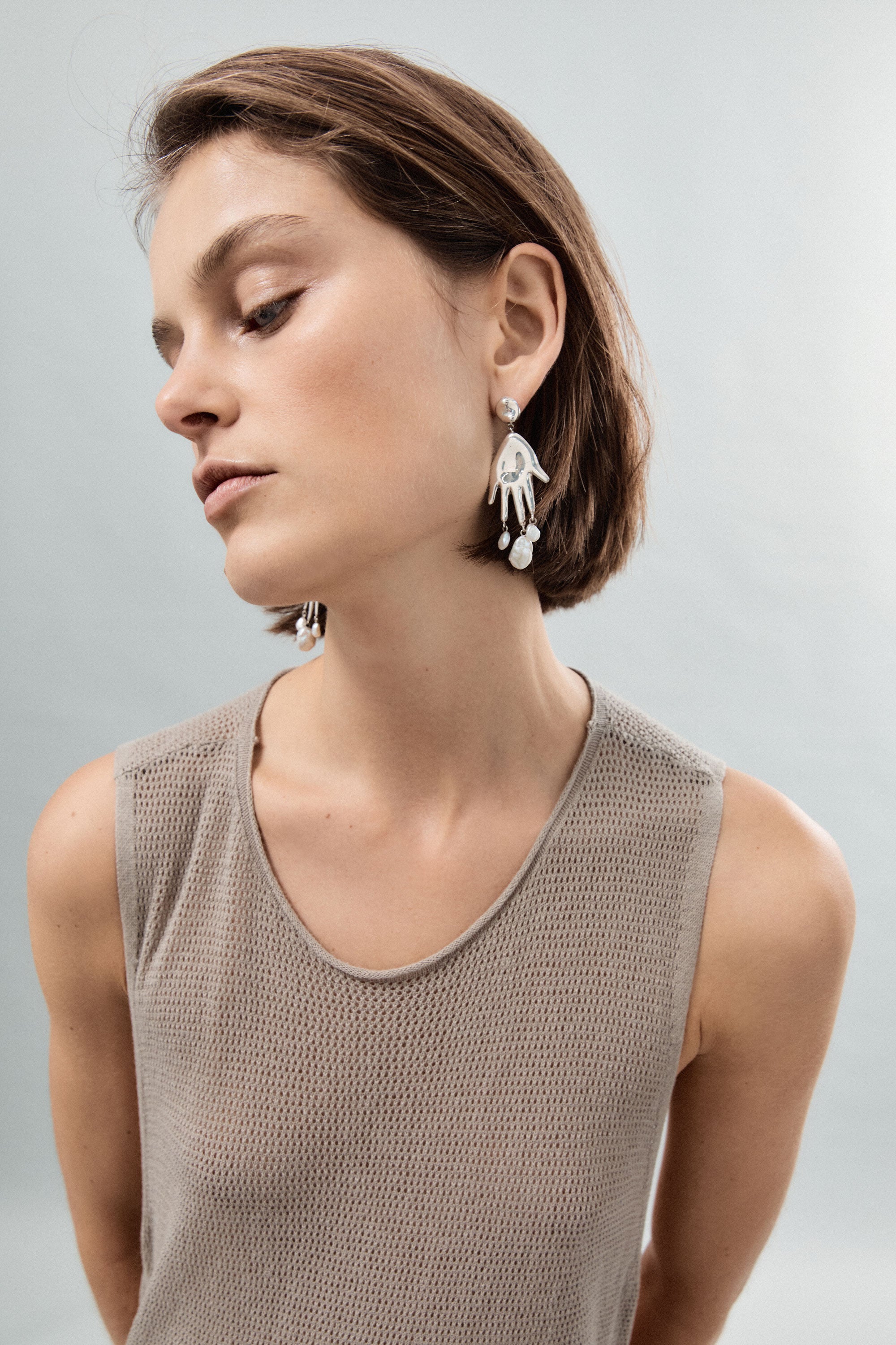 Woman wearing AGMES 0.925 sterling silver hand shaped earrings with pearl drops.