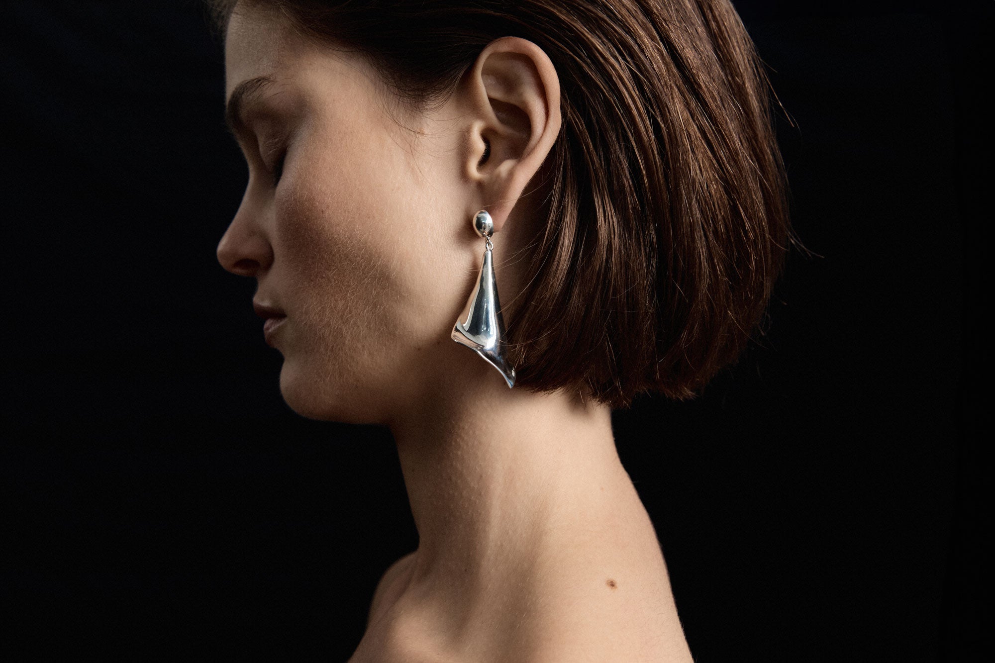 Model wearing AGMES .925 sterling silver Medium Calla drop Earrings. Black background.