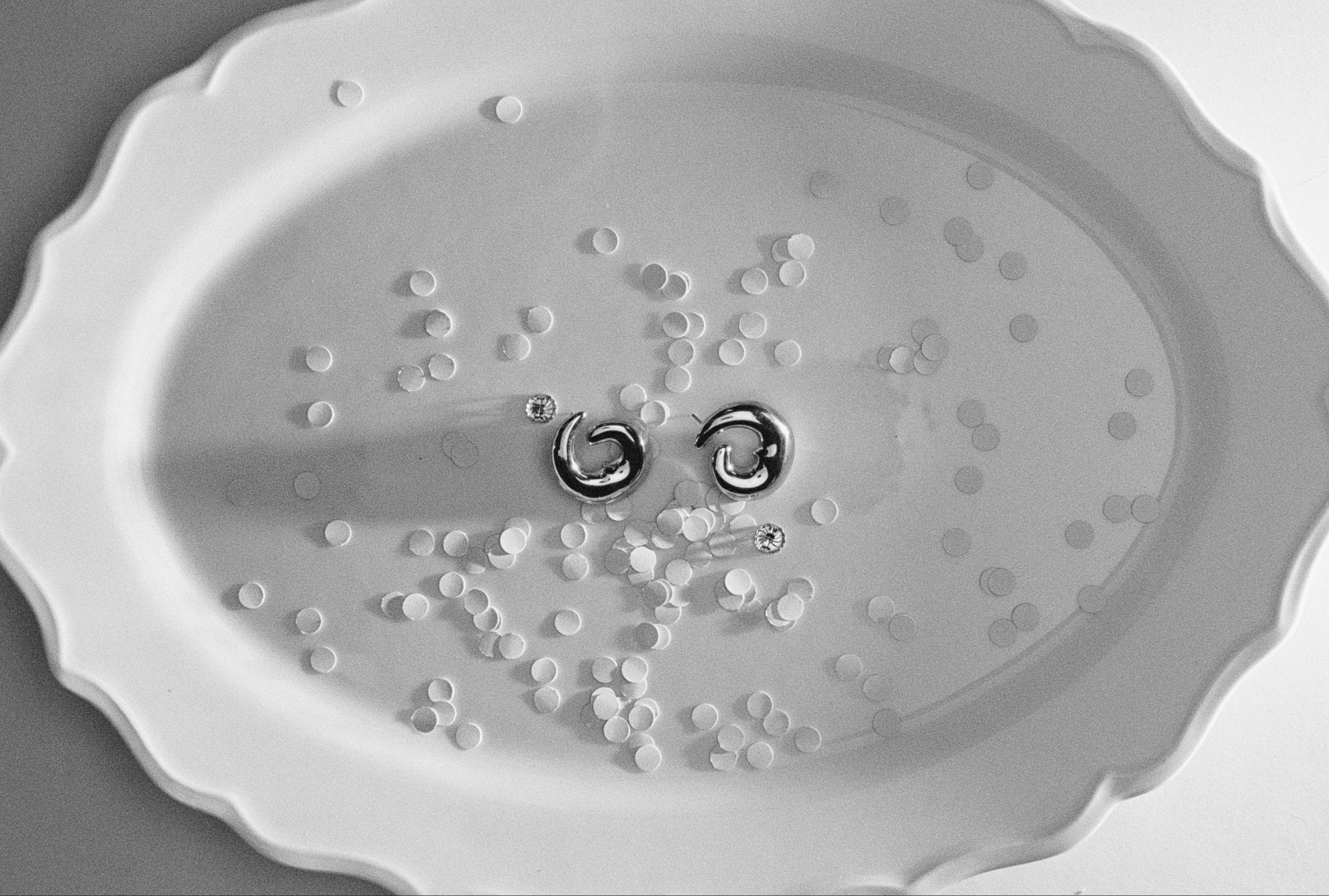 .925 sterling silver AGMES Nadia Hoop Earrings laying flat on a plate of confetti, still life
