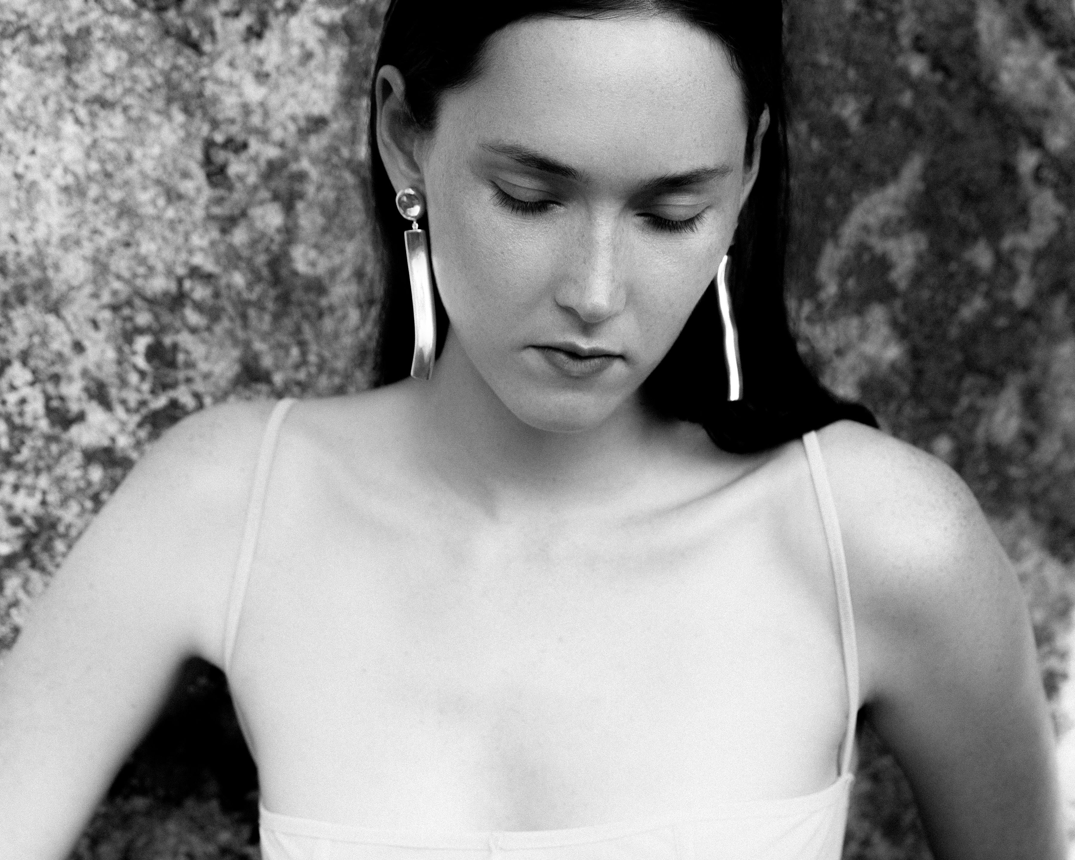 Woman wearing AGMES 0.925 sterling silver long sculptural drop earrings with silver top.
