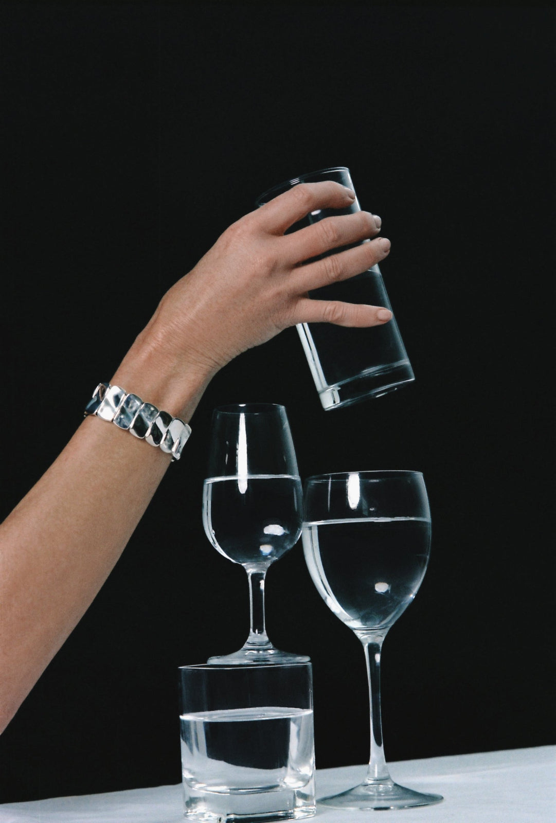 Model wearing AGMES .925 sterling silver sculptural paneled Short Ilona Bracelet holding glass of water on black background.