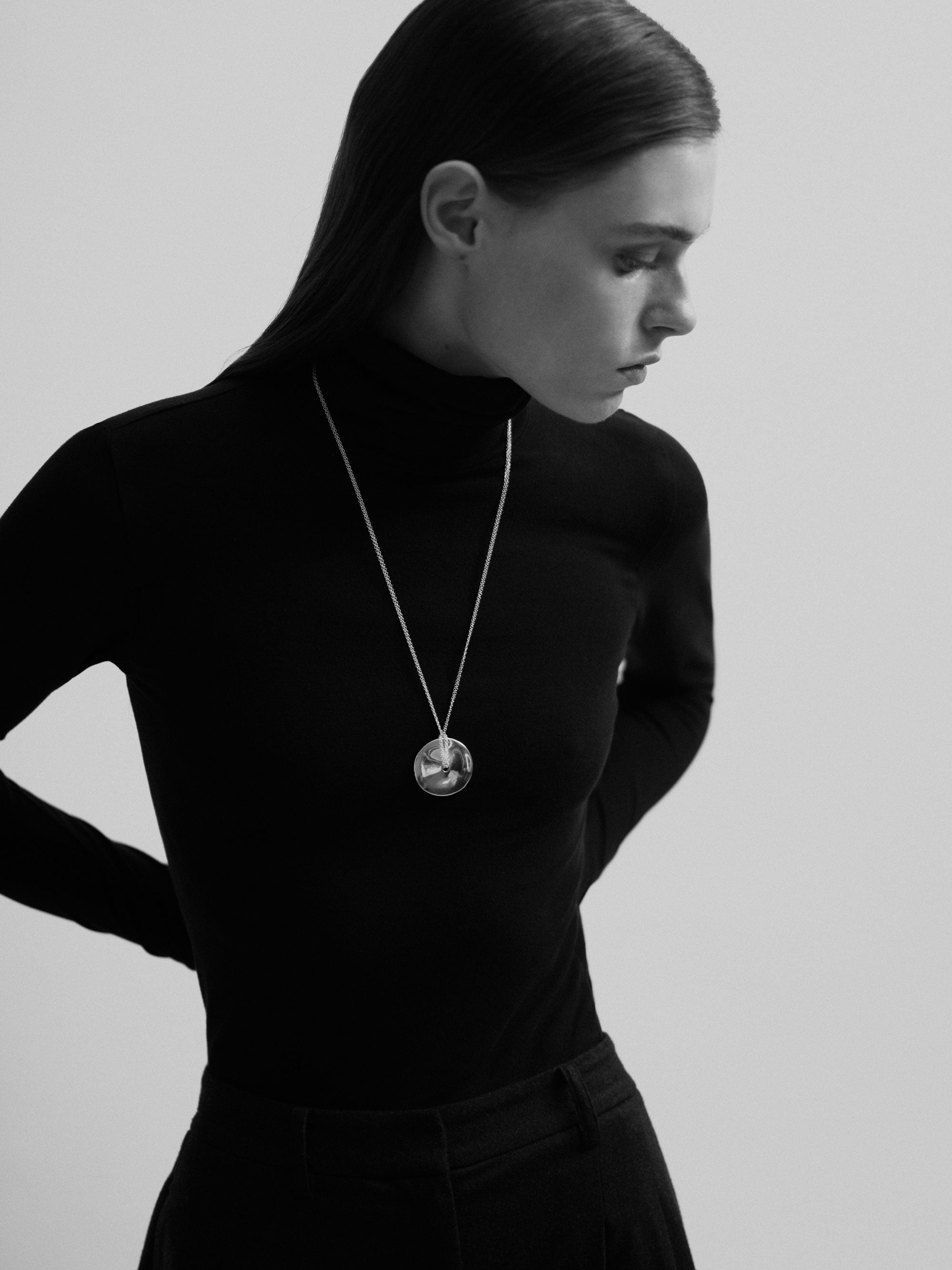 Model wearing 30 inch long circular cora pendant with .925 sterling silver double chain over black turtleneck