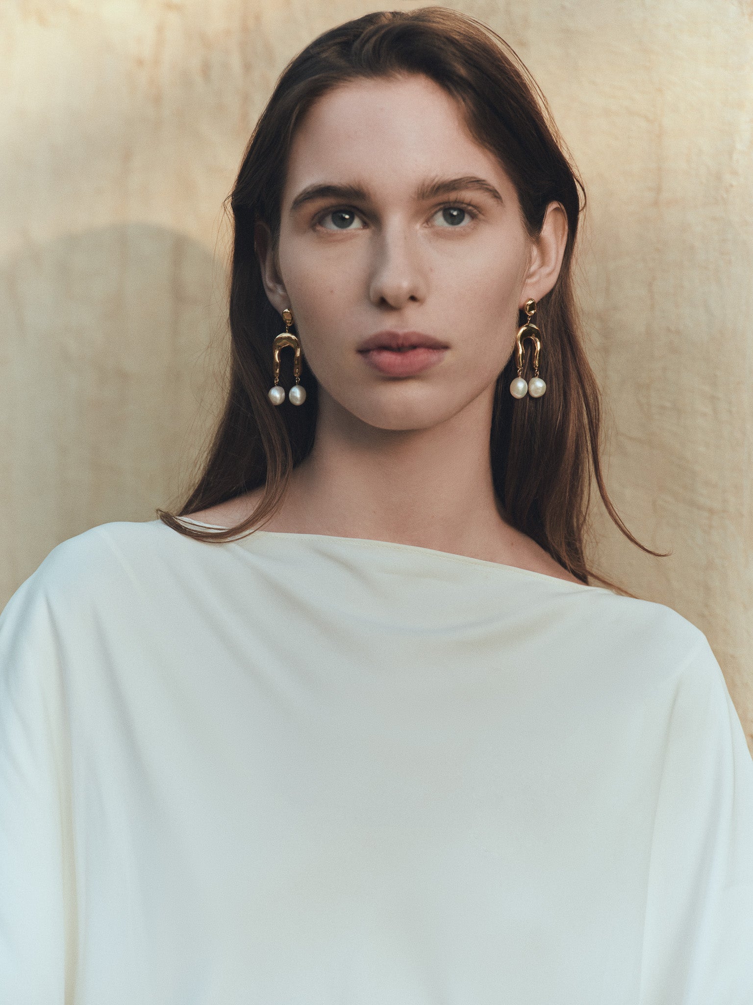 Woman wearing AGMES 18k gold vermeil earrings with sculpted wishbone and freshwater pearl drop.