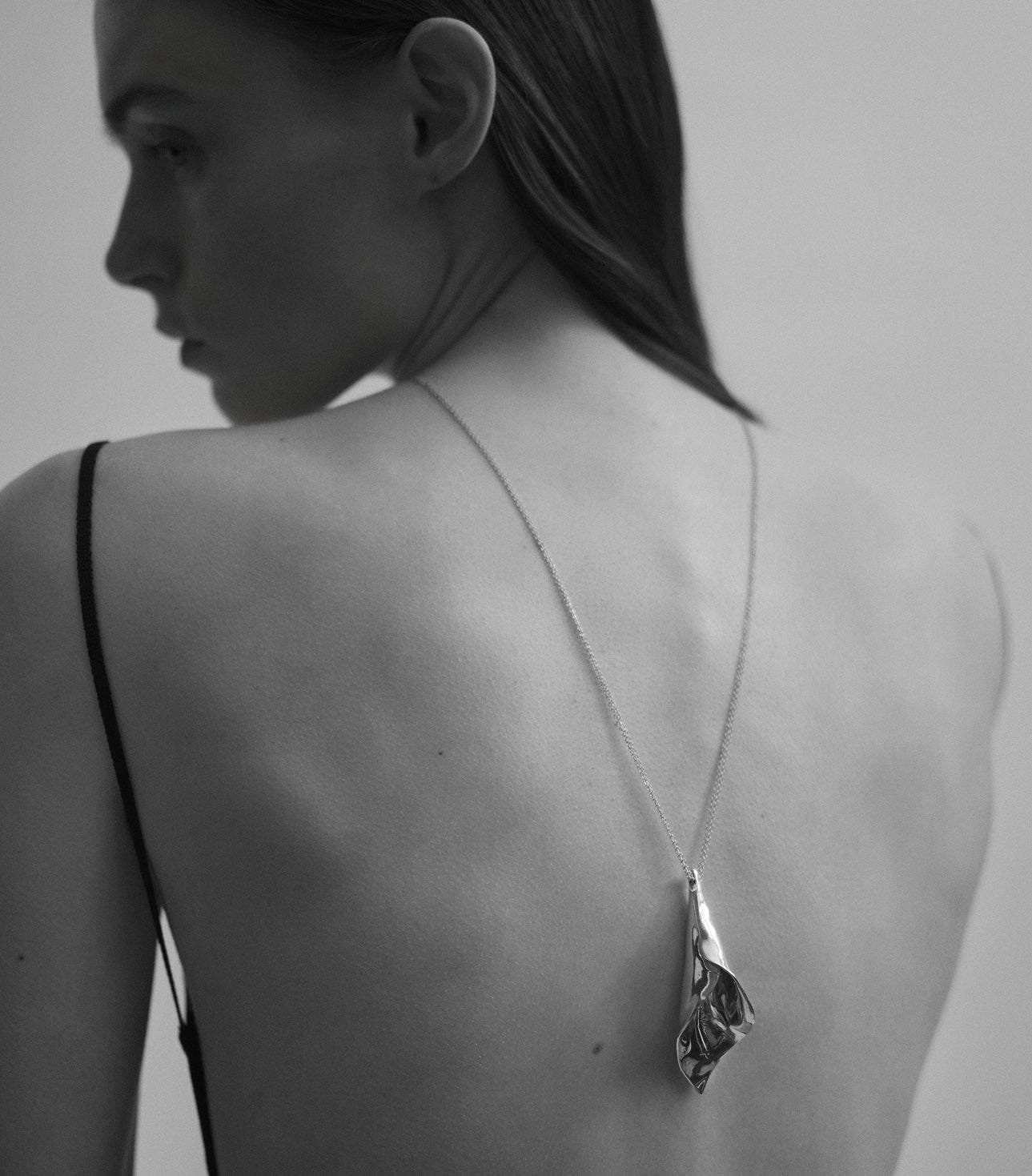 Model wearing AGMES .925 sterling silver organic sculptural Calla Pendant necklace on back. Black and white image.
