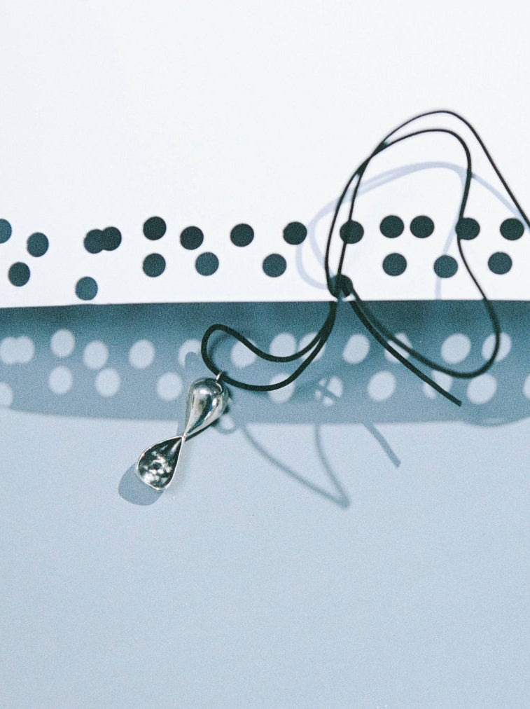 AGMES .925 sterling silver Inti infinity shaped pendant necklace on black suede cord. Pendant is on light blue background with cord string through holes in white paper.
