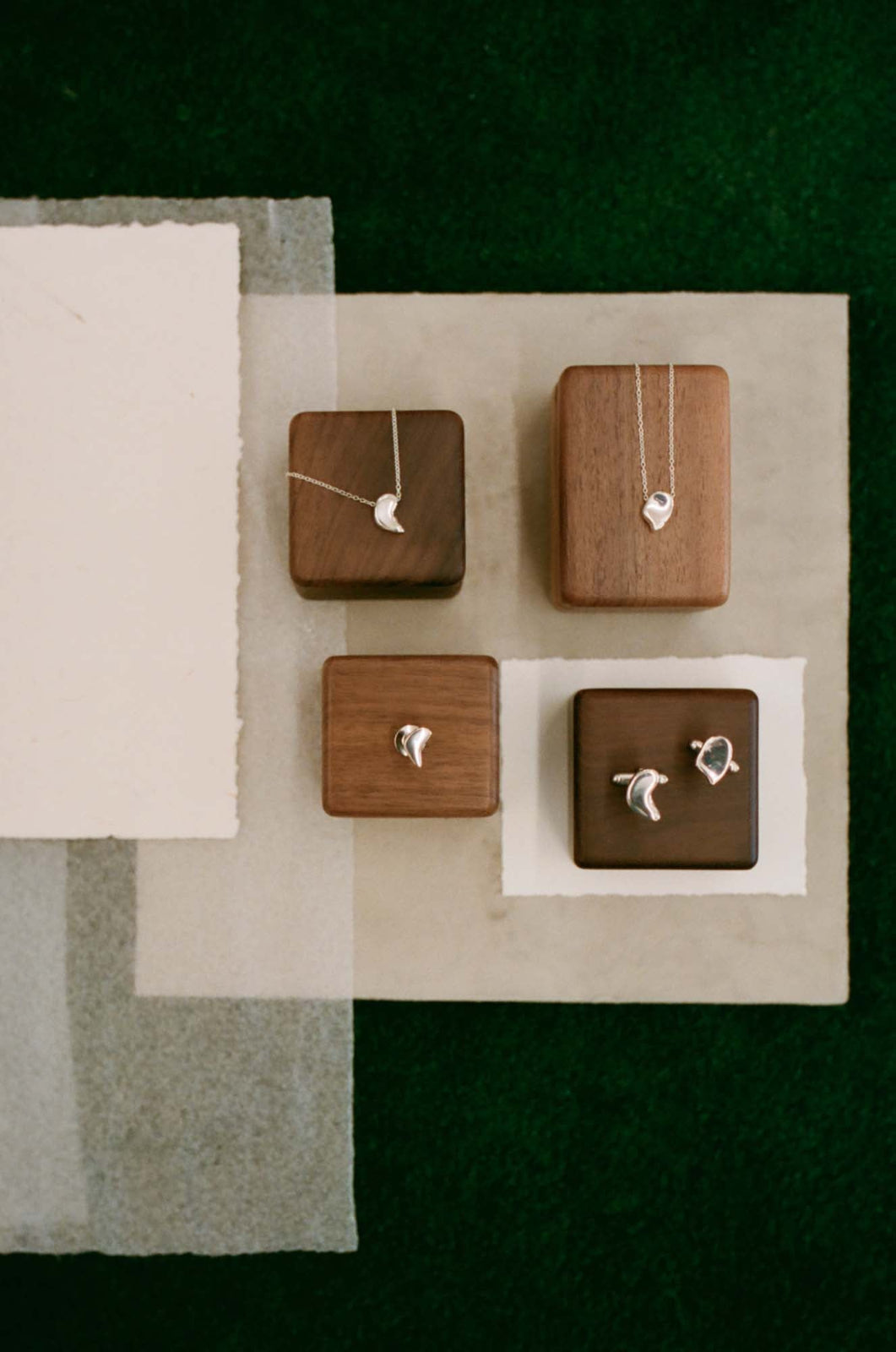 AGMES .925 sterling silver sculptural heart shaped sum of parts pendant set, mini brooch, and cufflinks. Layered on square wooden blocks, white paper, and green background.