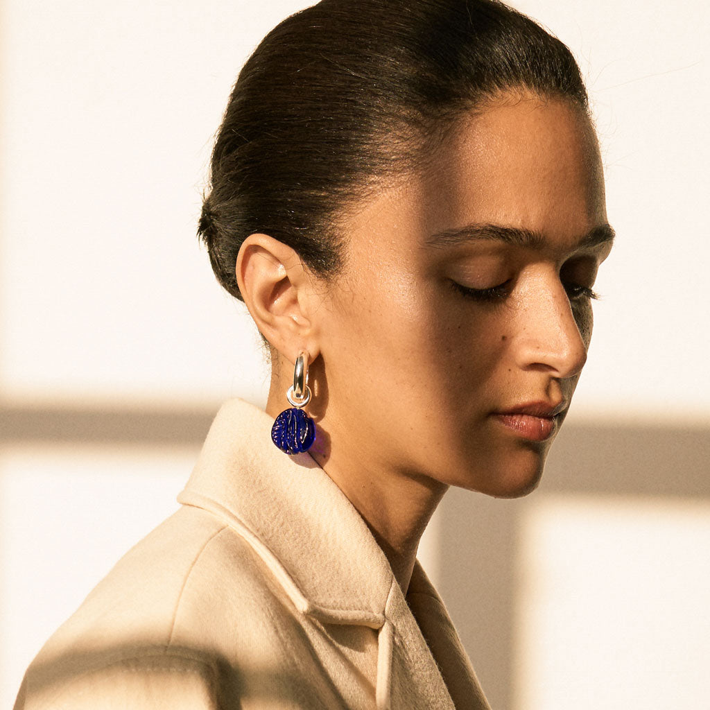 Woman wearing AGMES .925 sterling silver hoop earrings with blue glass bead drop.