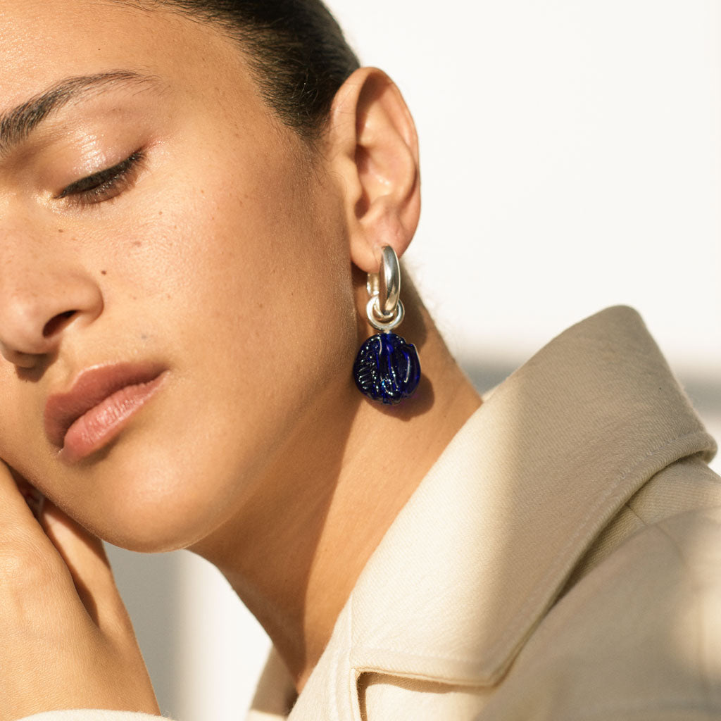 Person wearing AGMES .925 sterling silver hoop earrings with blue glass bead drop.