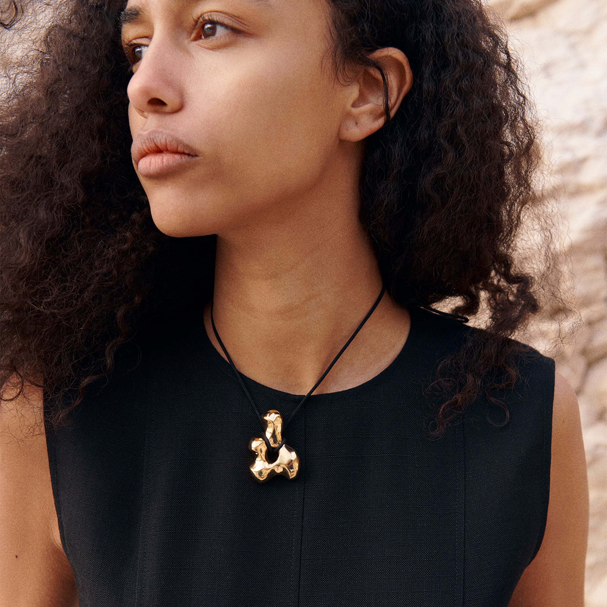 Woman wearing AGMES 18k Gold Vermeil sculpted pendant on black suede cord. Simone Bodmer-Turner.
