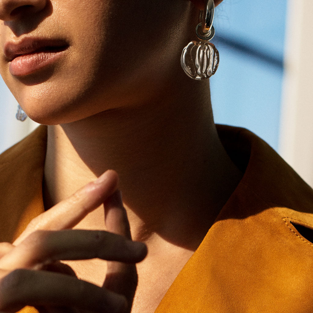 Person wearing AGMES .925 sterling silver hoop earrings with clear glass bead drop.