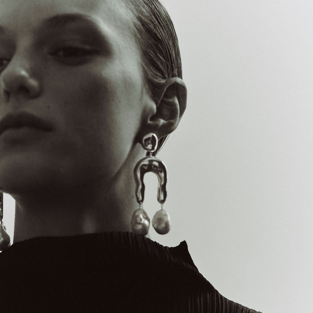 Woman wearing AGMES 0.925 sterling silver earrings with sculpted wishbone and freshwater pearl drop.