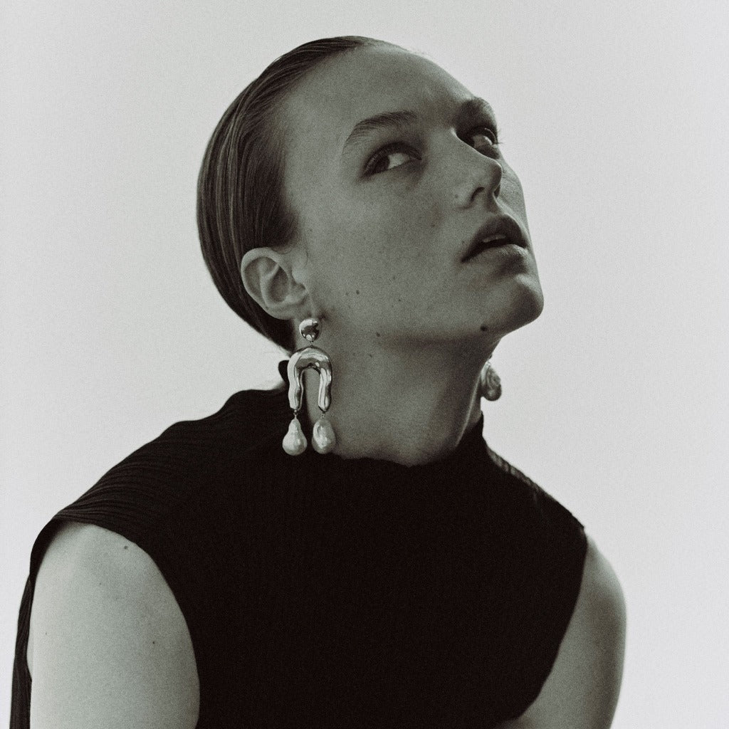 Woman wearing AGMES 0.925 sterling silver earrings with sculpted wishbone and freshwater pearl drop.