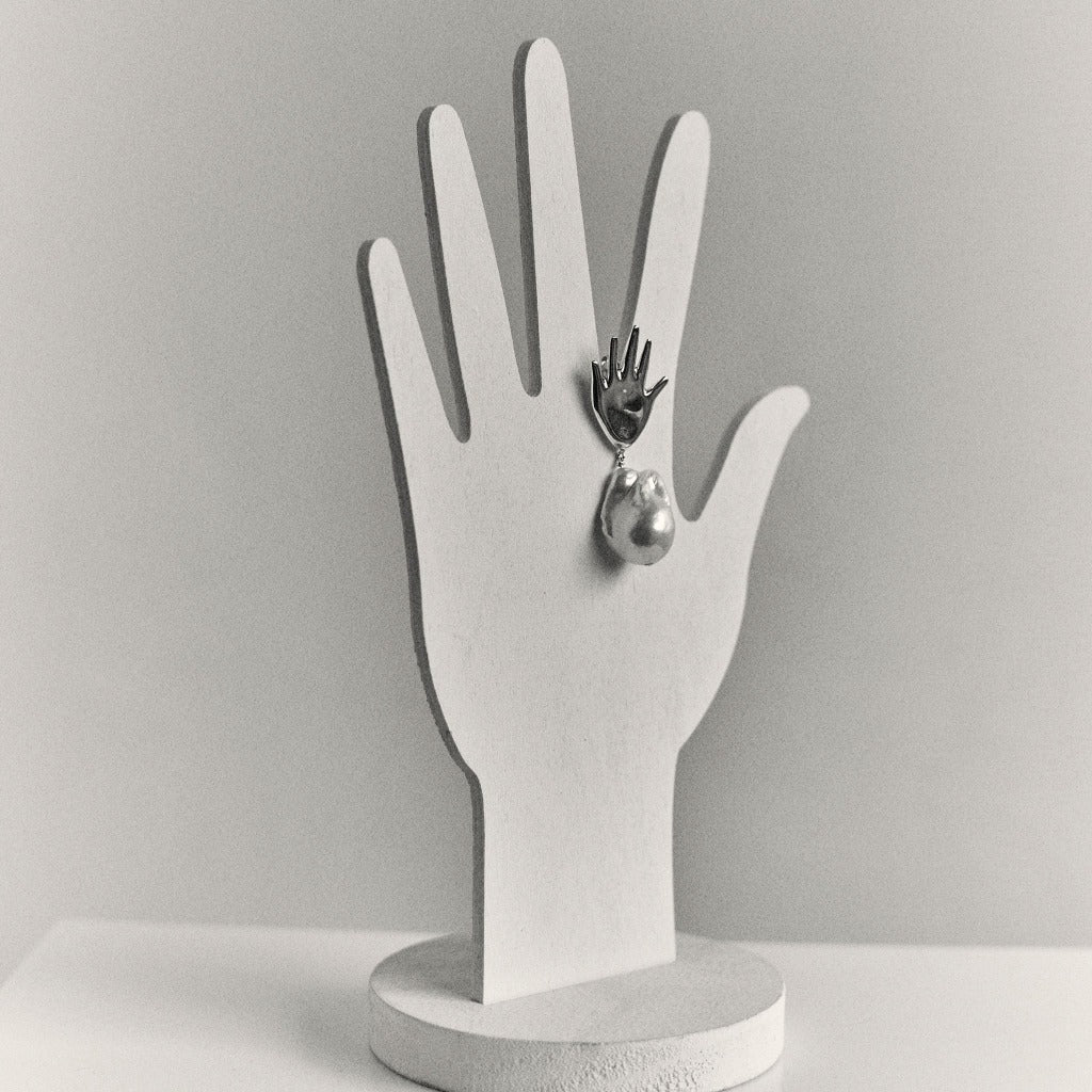 AGMES 0.925 sterling silver abstract hand earrings with baroque freshwater pearl drop displayed on white hand stand.