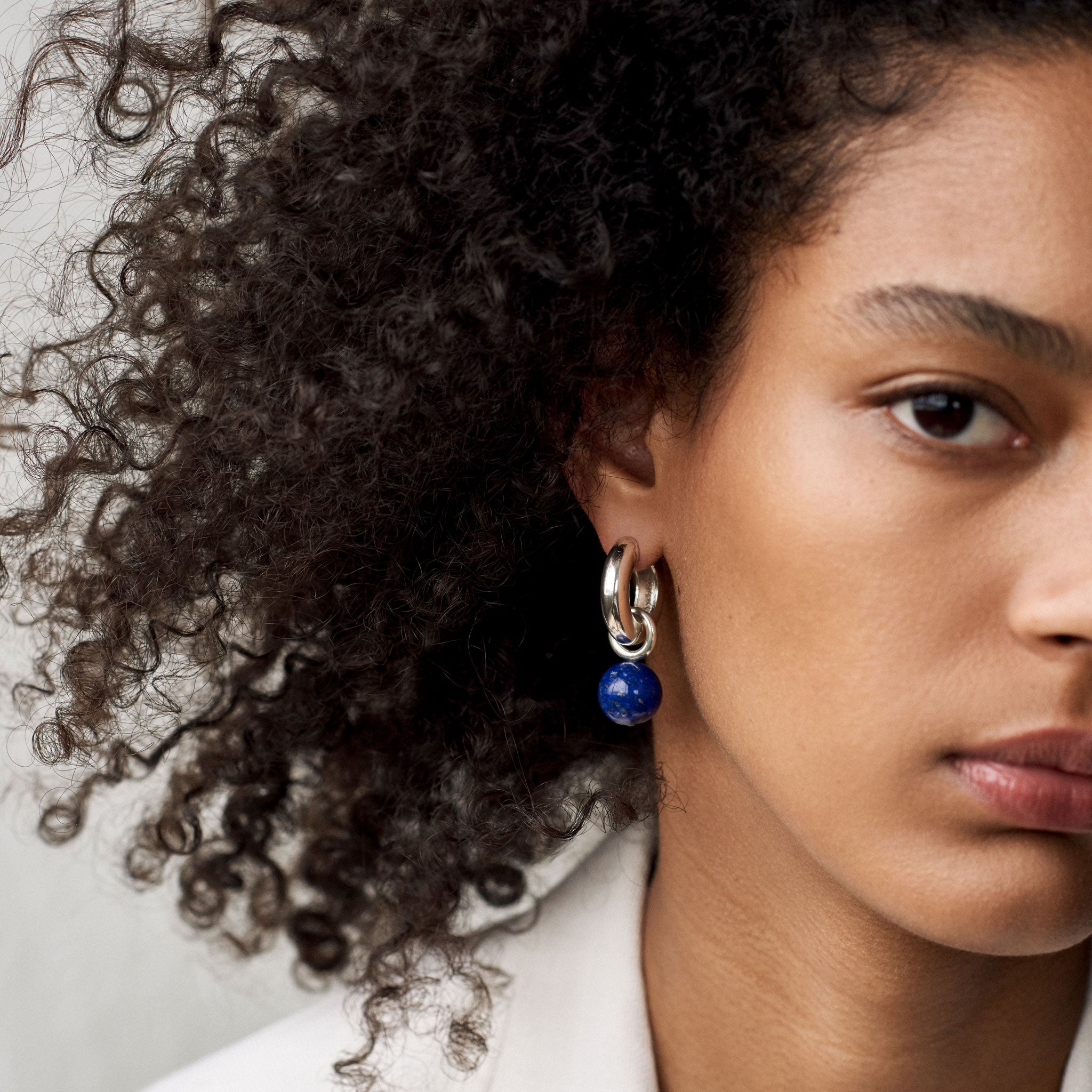 Woman wearing AGMES 0.925 sterling silver Sonia hoops with lapis drop embellishments.