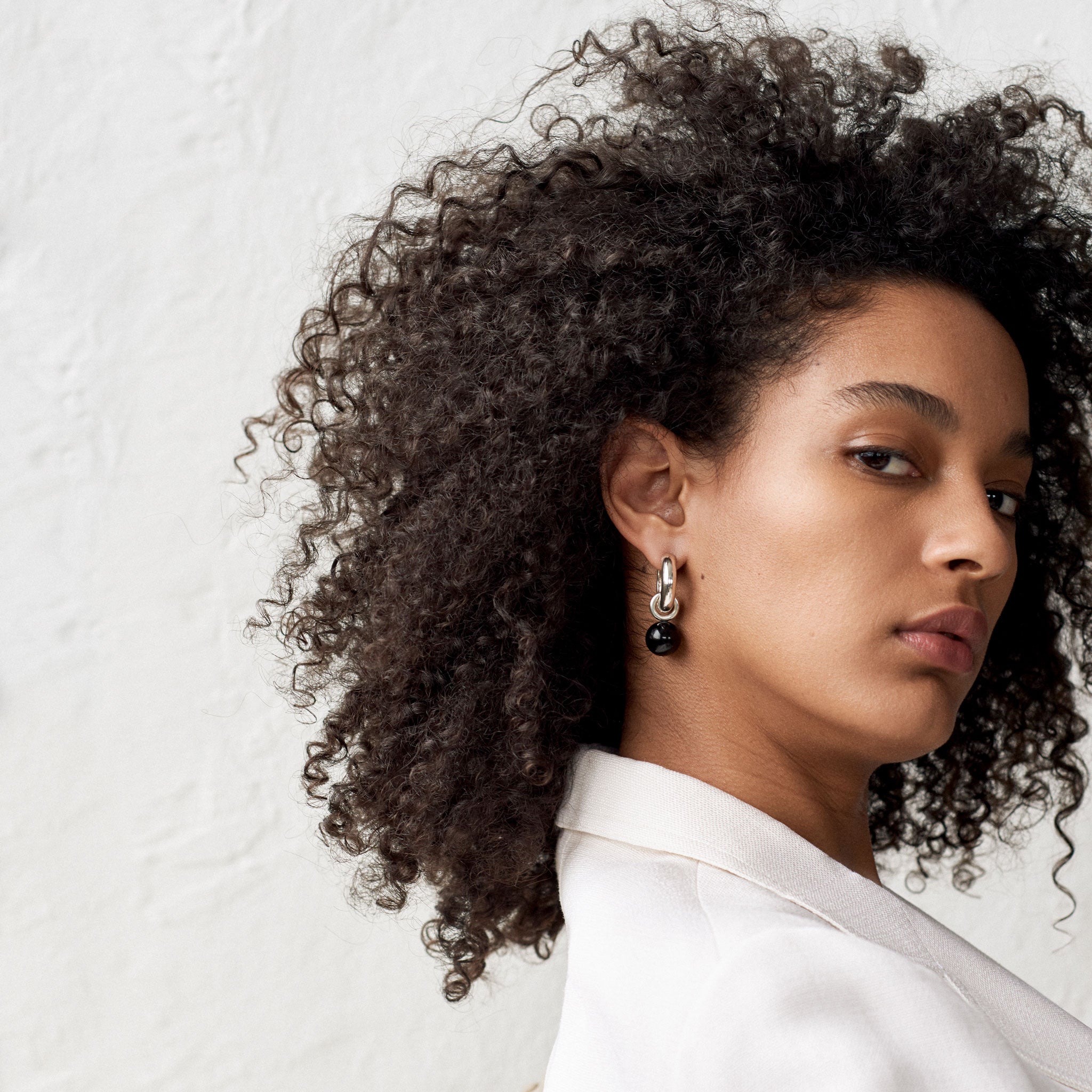 Woman wearing AGMES 0.925 sterling silver Sonia hoops with onyx drop embellishments.