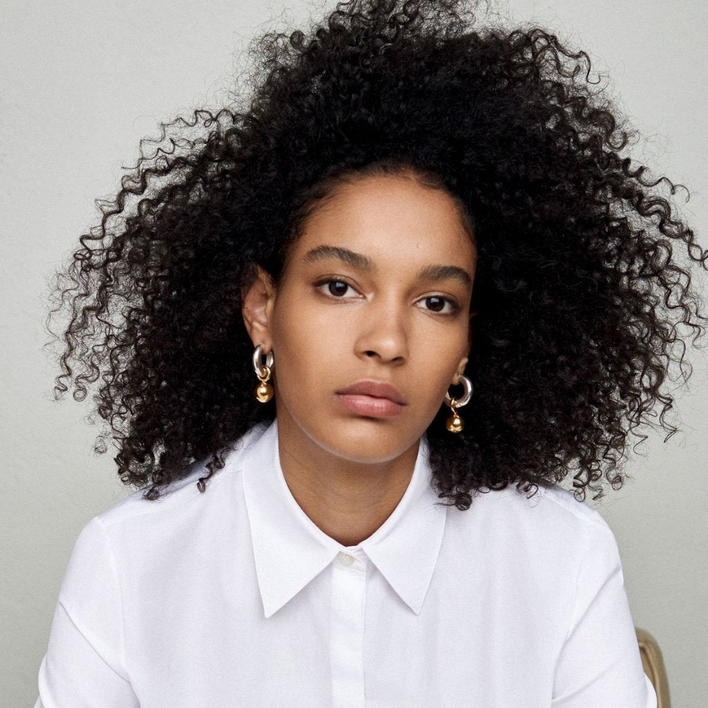 Woman wearing AGMES 0.925 sterling silver hinged hoop earrings with 18k yellow gold round embellishments.