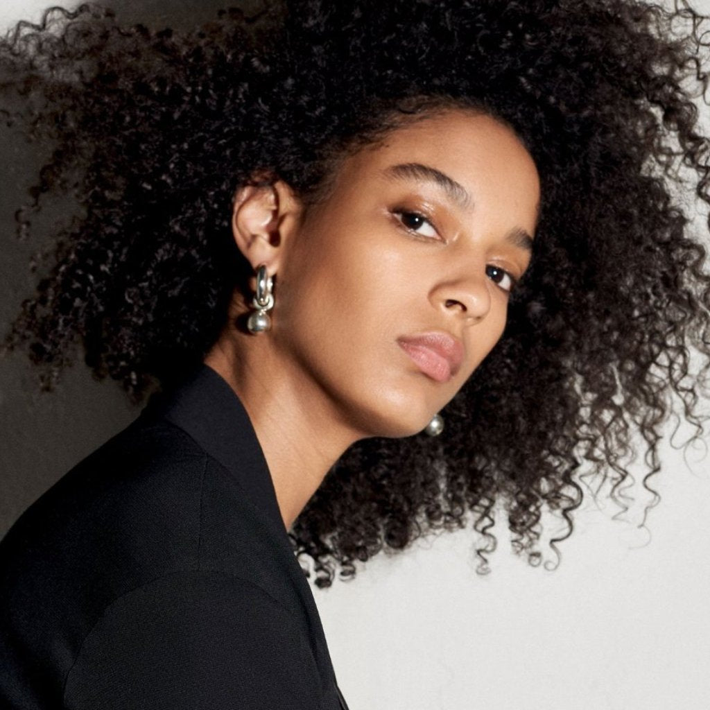 Woman wearing AGMES 0.925 sterling silver hinged hoop earrings with 18k yellow gold round embellishments.