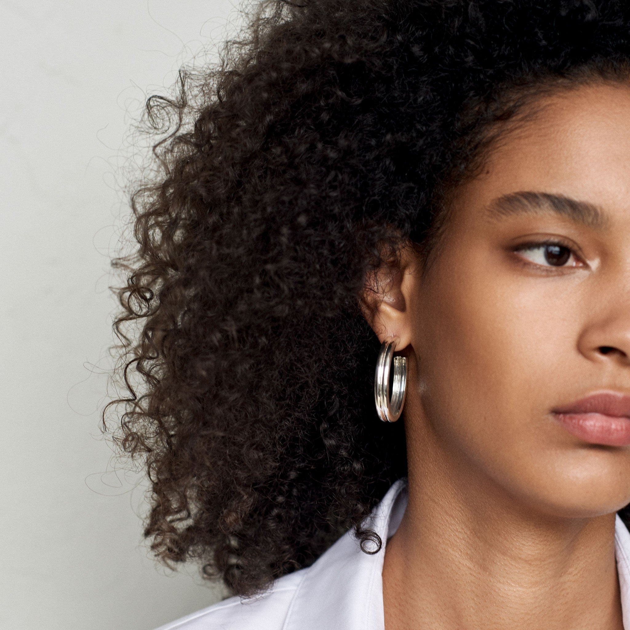 Woman wearing AGMES 0.925 sterling silver double ridged large hoop earrings.