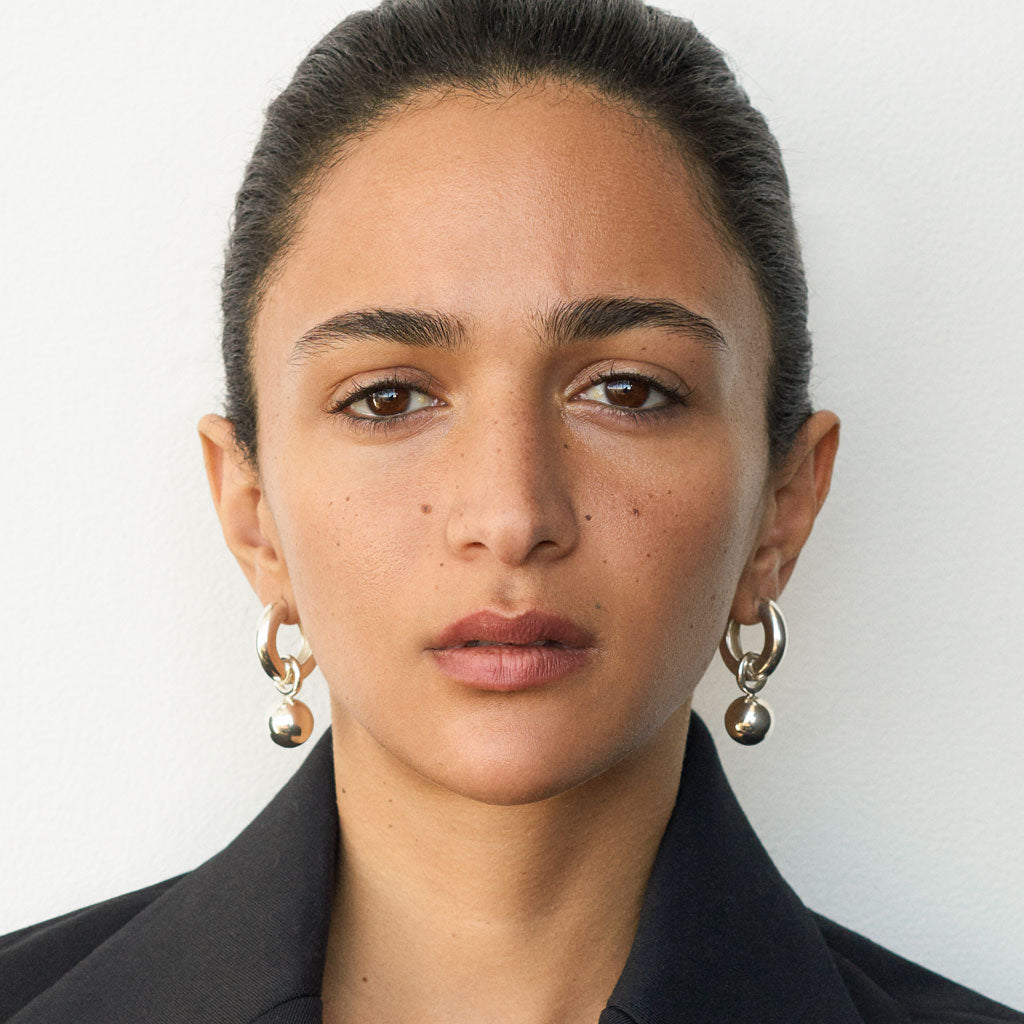 Woman wearing AGMES 0.925 sterling silver hinged hoop earrings with 18k yellow gold round embellishments.