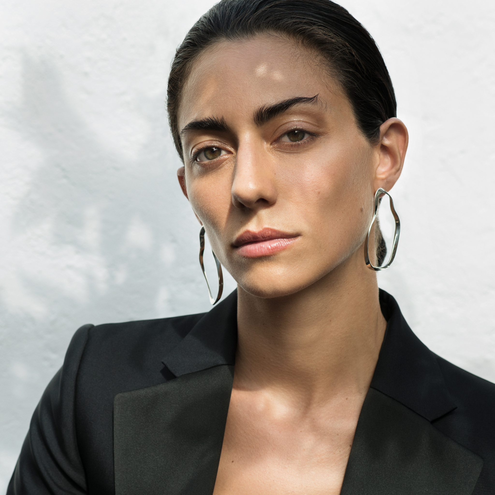 Woman wearing AGMES 0.925 sterling silver sculptural wavy round hoop earrings.