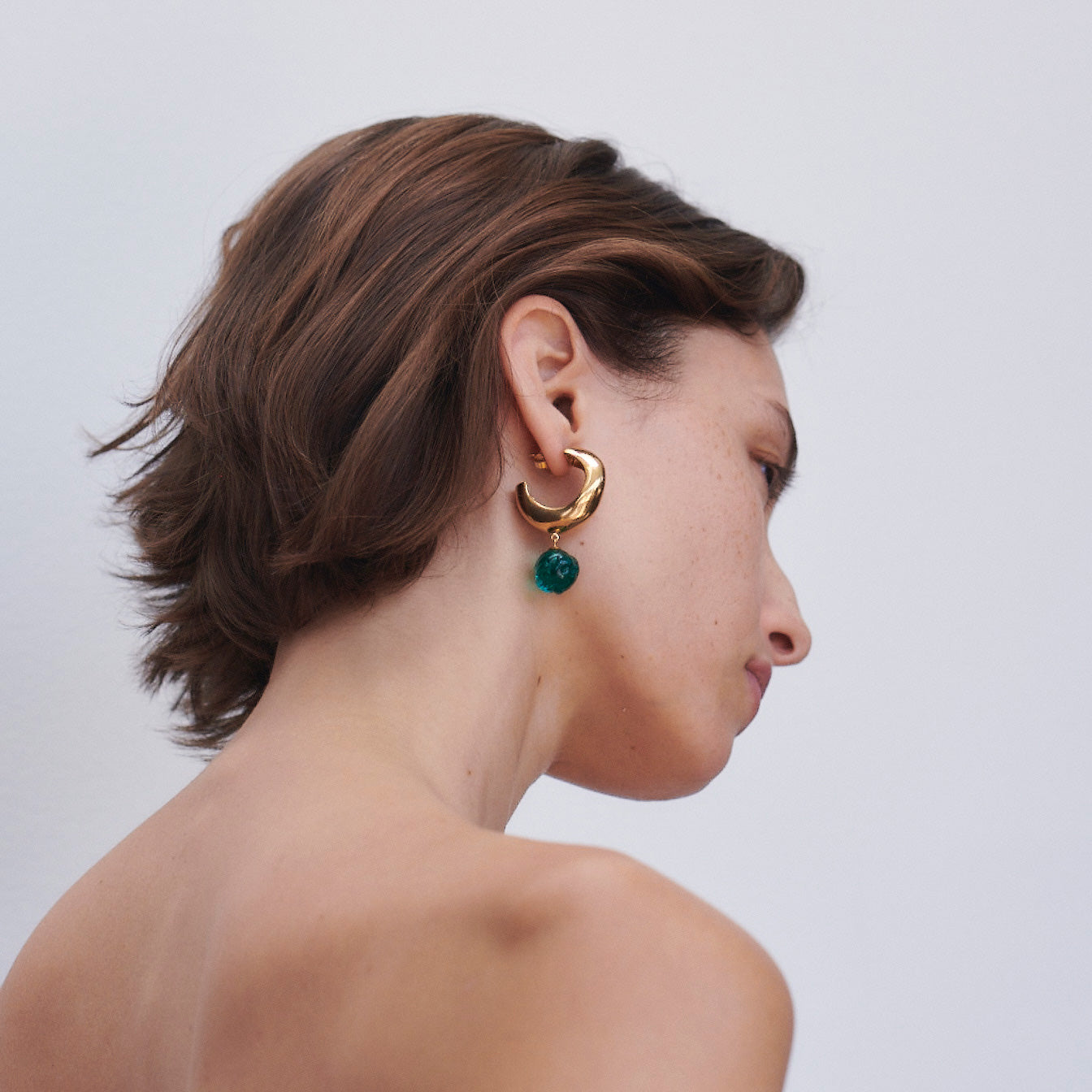 Woman wearing AGMES yellow gold vermeil Cleo hoop earrings with green glass beads.
