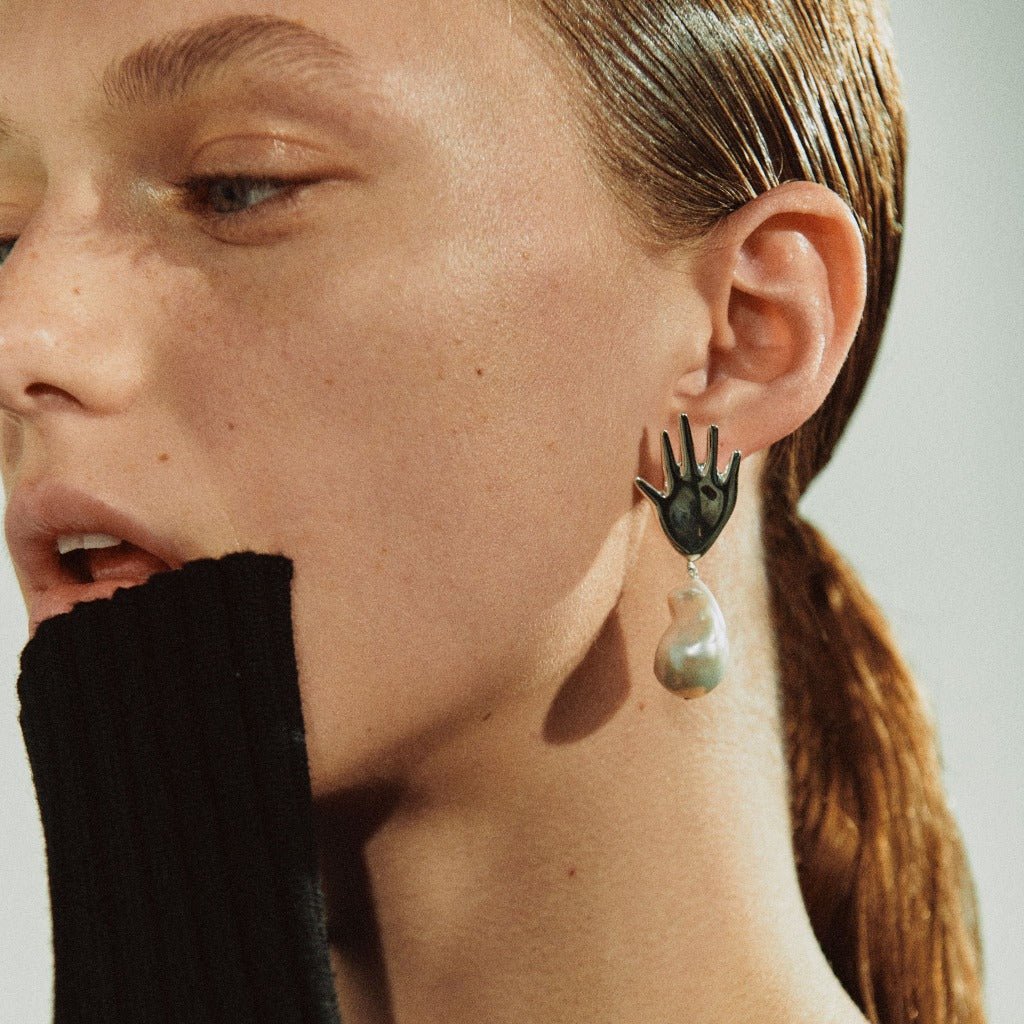 Woman wearing AGMES 0.925 sterling silver abstract hand earrings with baroque freshwater pearl drop.