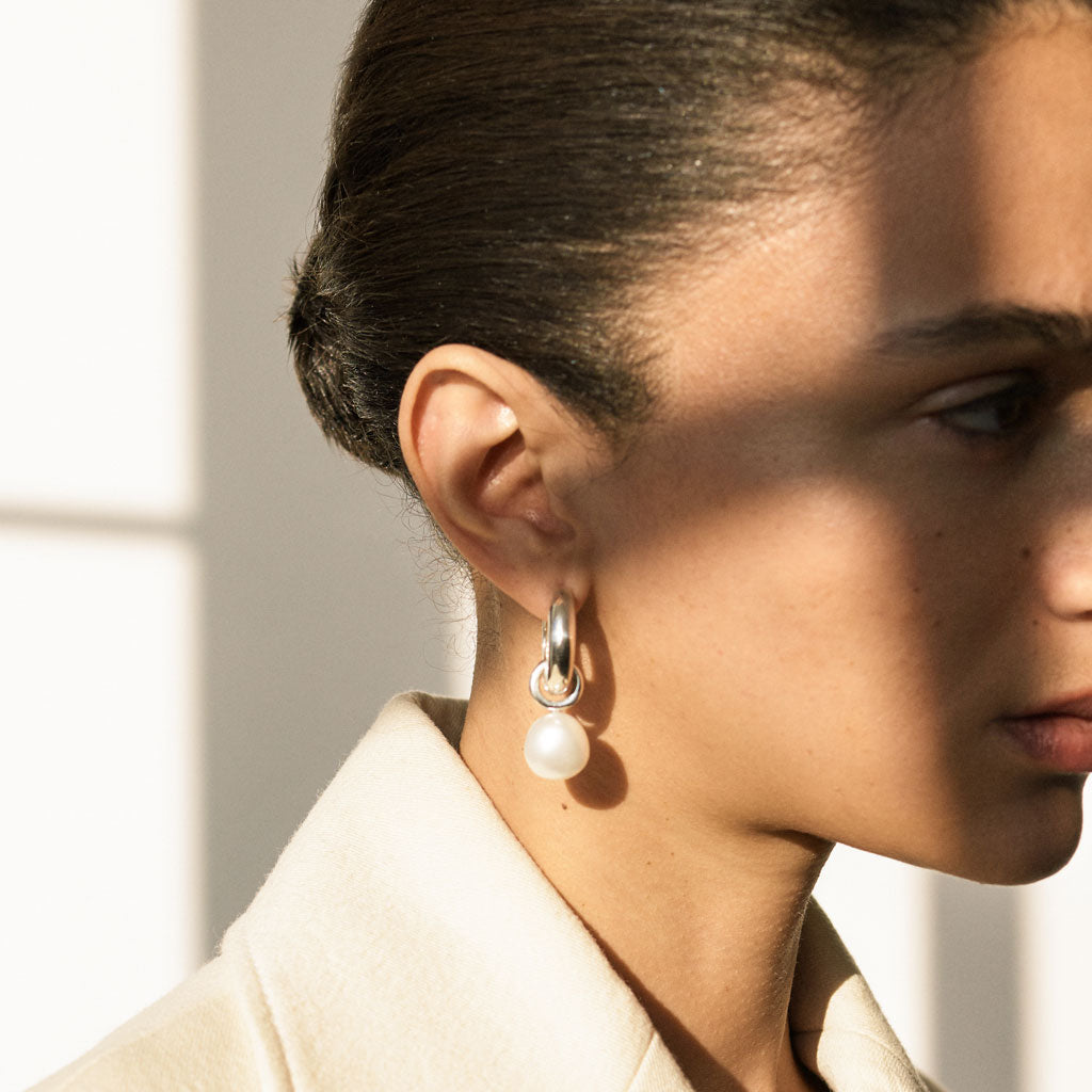 Woman wearing AGMES 0.925 sterling silver hinged hoop earrings with freshwater pearl drop embellishments.
