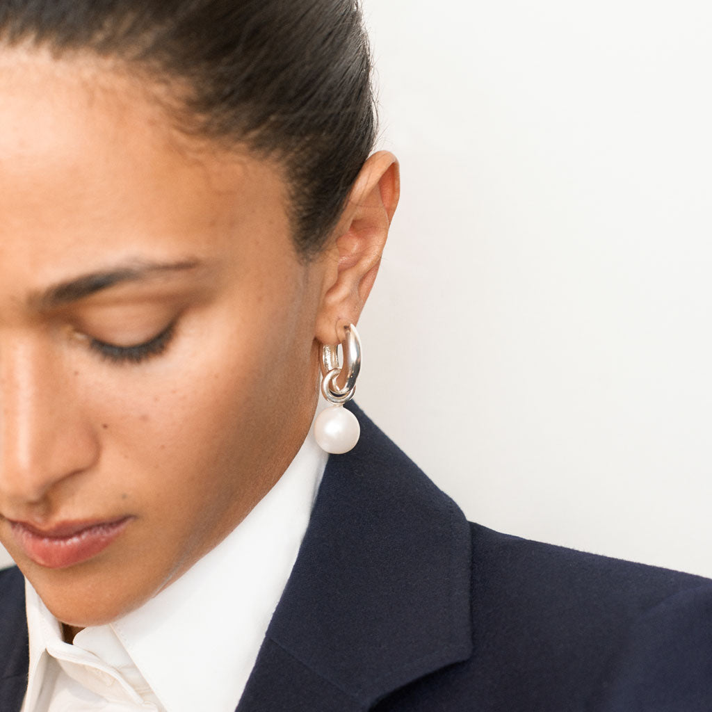 Woman wearing AGMES 0.925 sterling silver hinged hoop earrings with freshwater pearl drop embellishments.