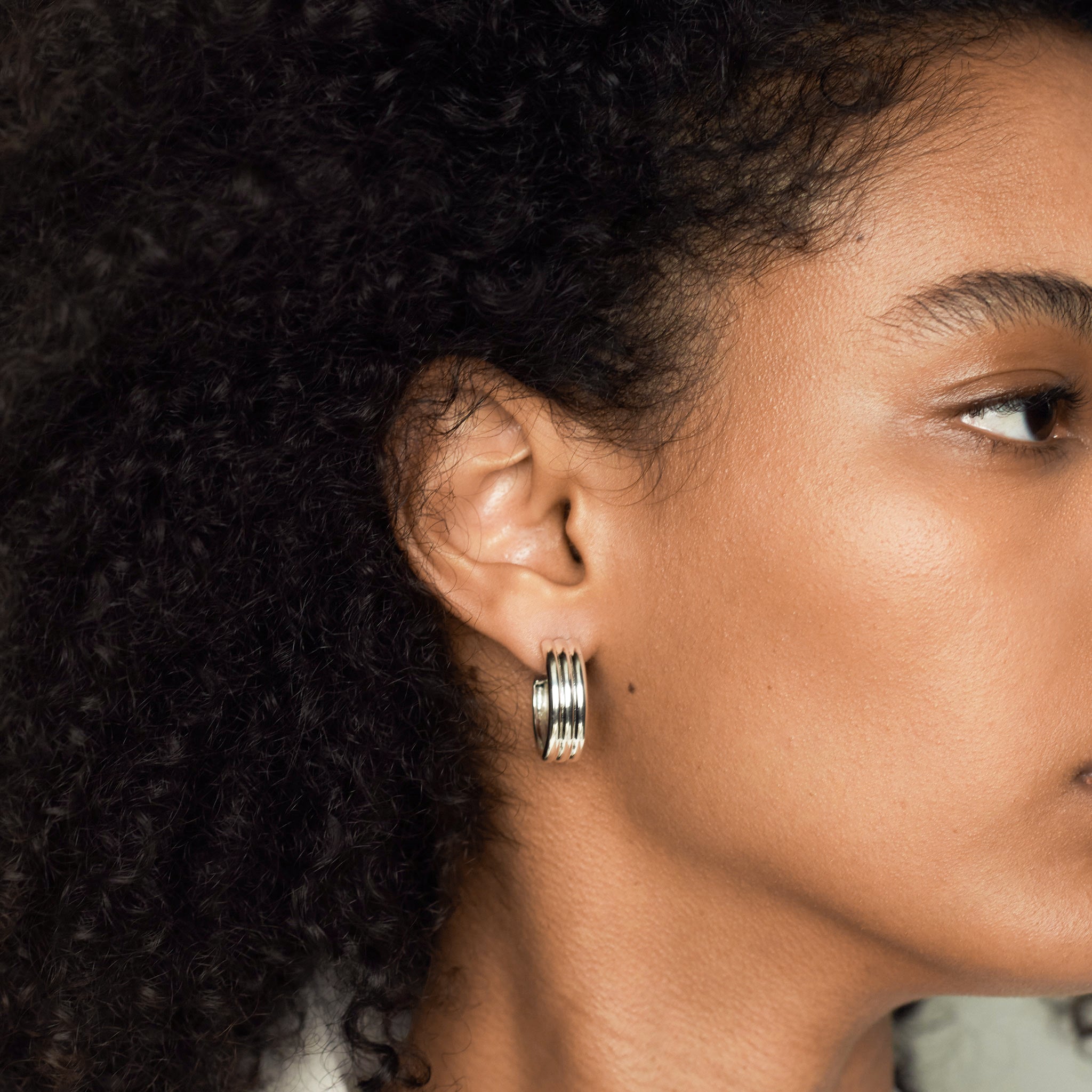 Woman wearing AGMES 0.925 sterling silver triple ridged medium hoop earrings.
