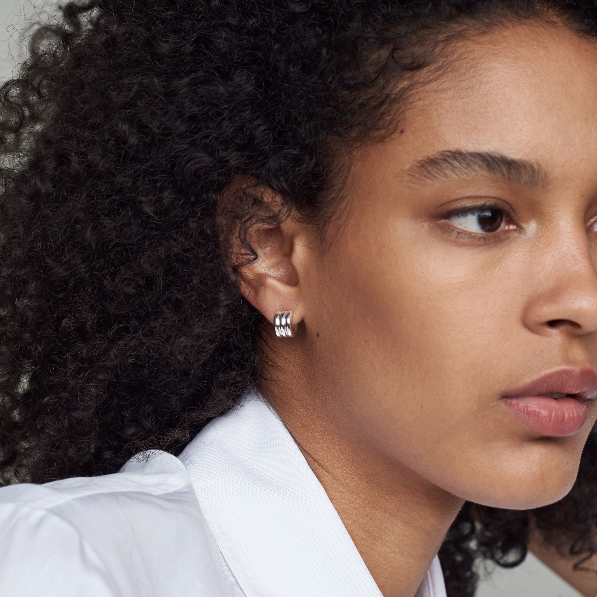 Woman wearing AGMES 0.925 sterling silver triple ridged mini hoop earrings.